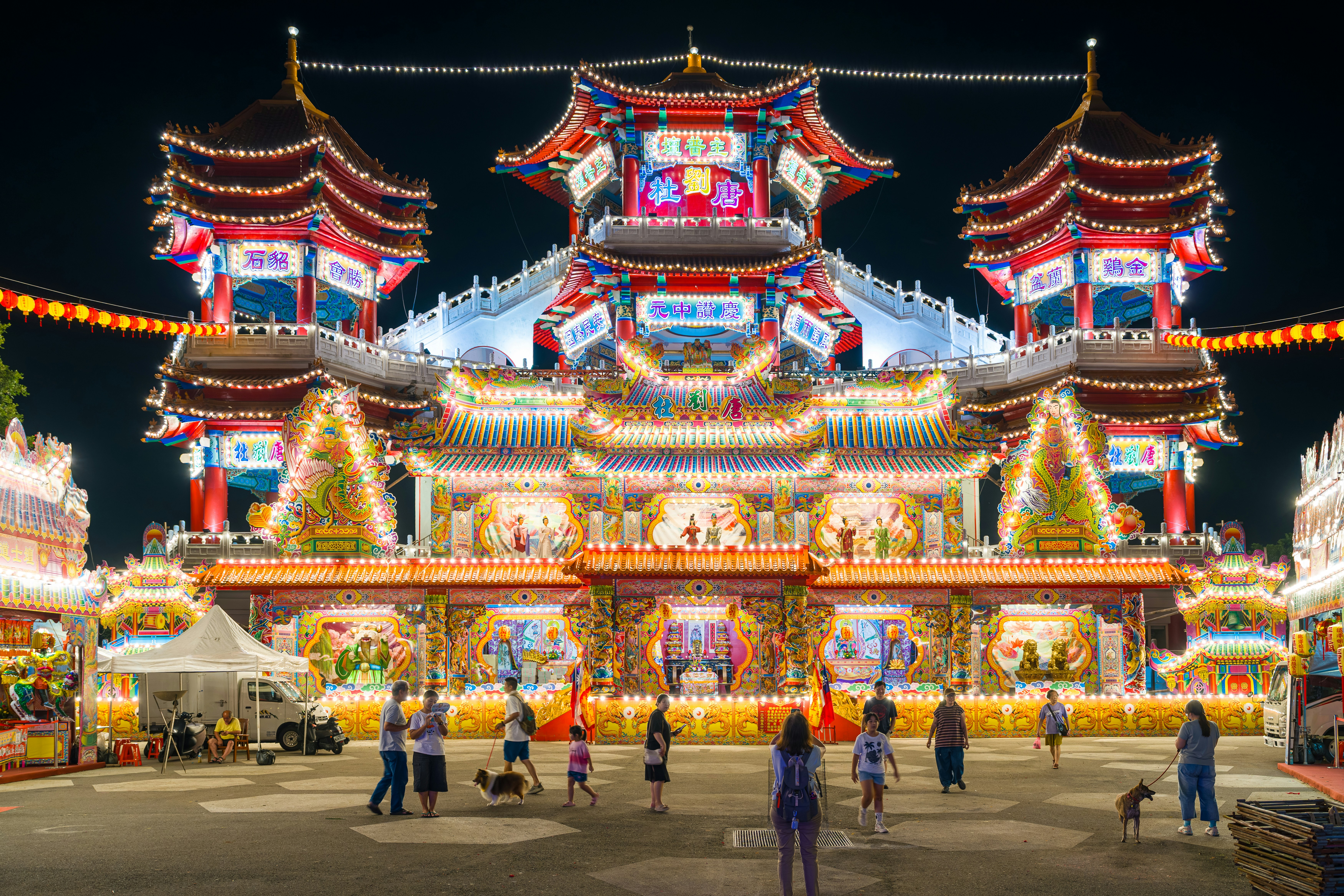 People walking in front of a brightly illuminated traditional temple at night
