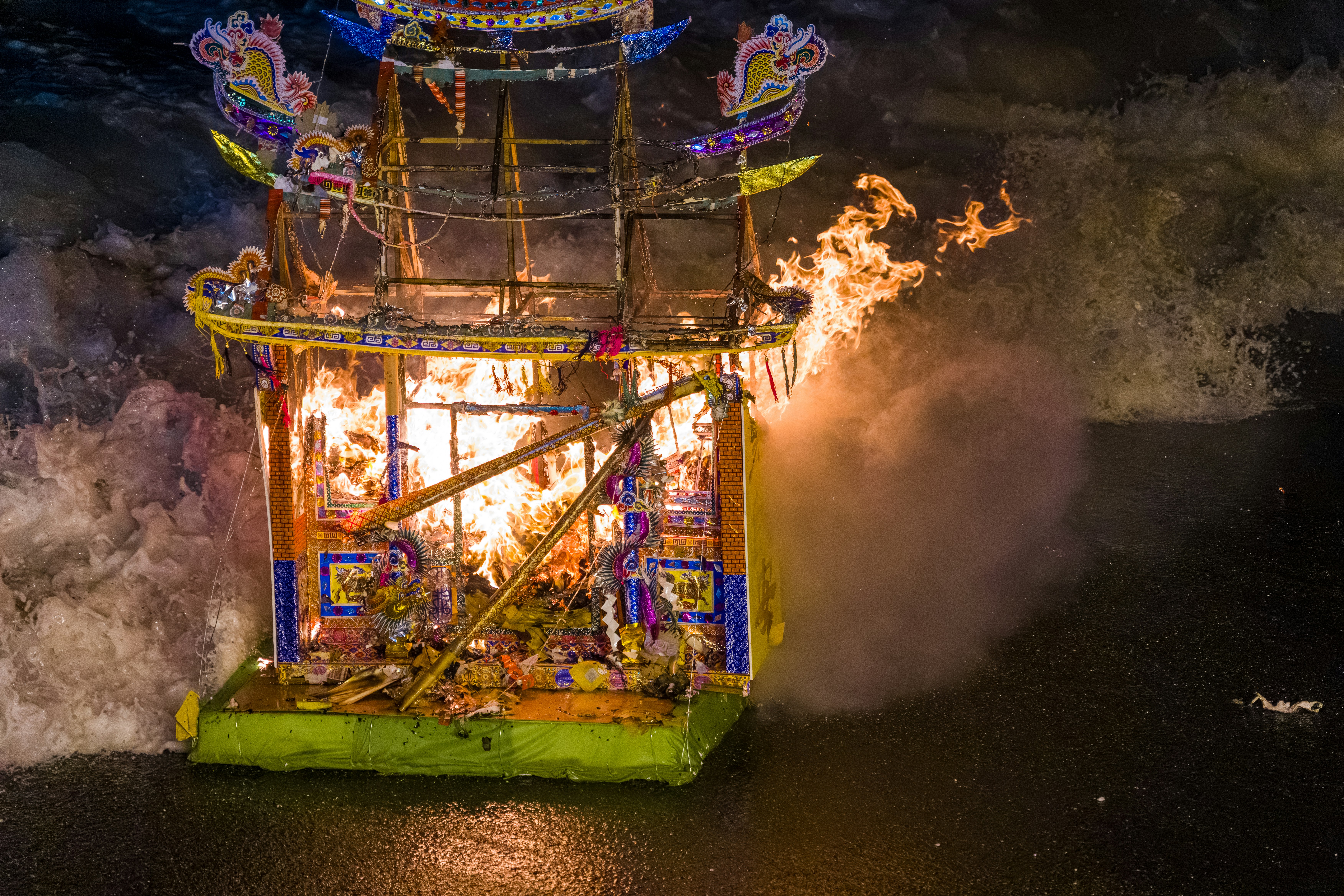 A decorative paper structure burning on a dark wet surface with splashing water