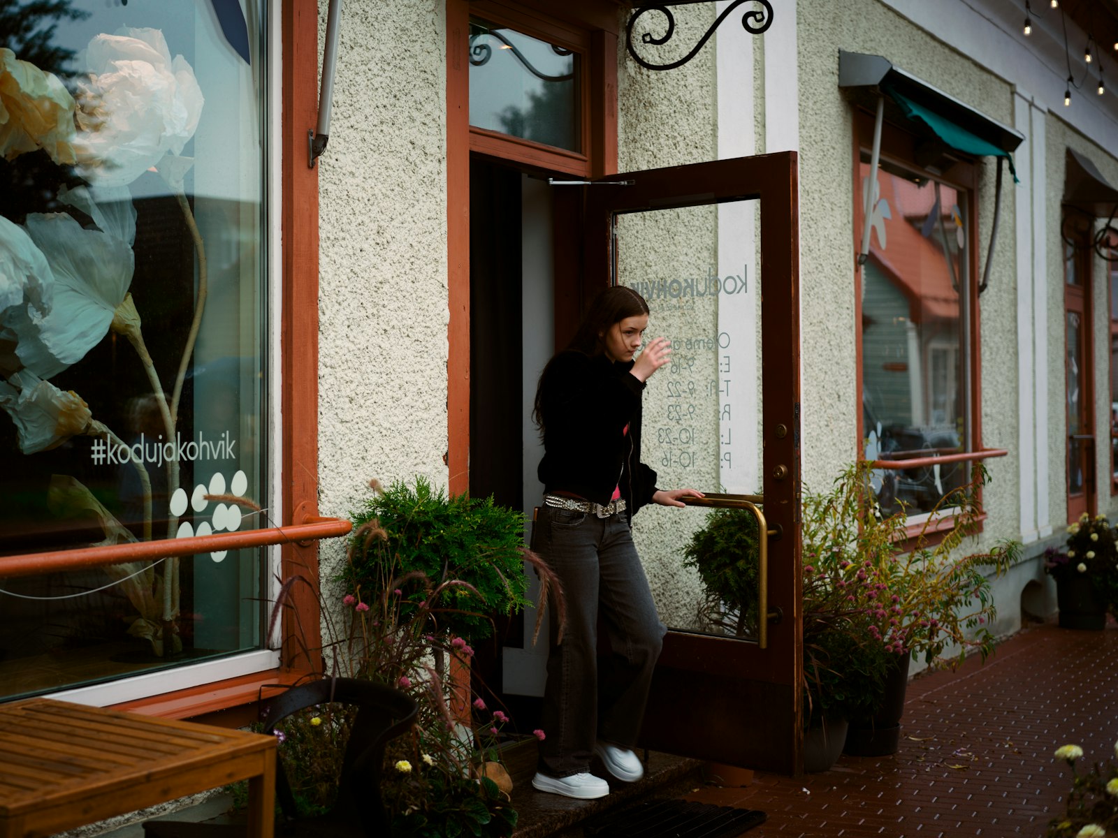 Mulher sai pela porta de um café de esquina com plantas na entrada.