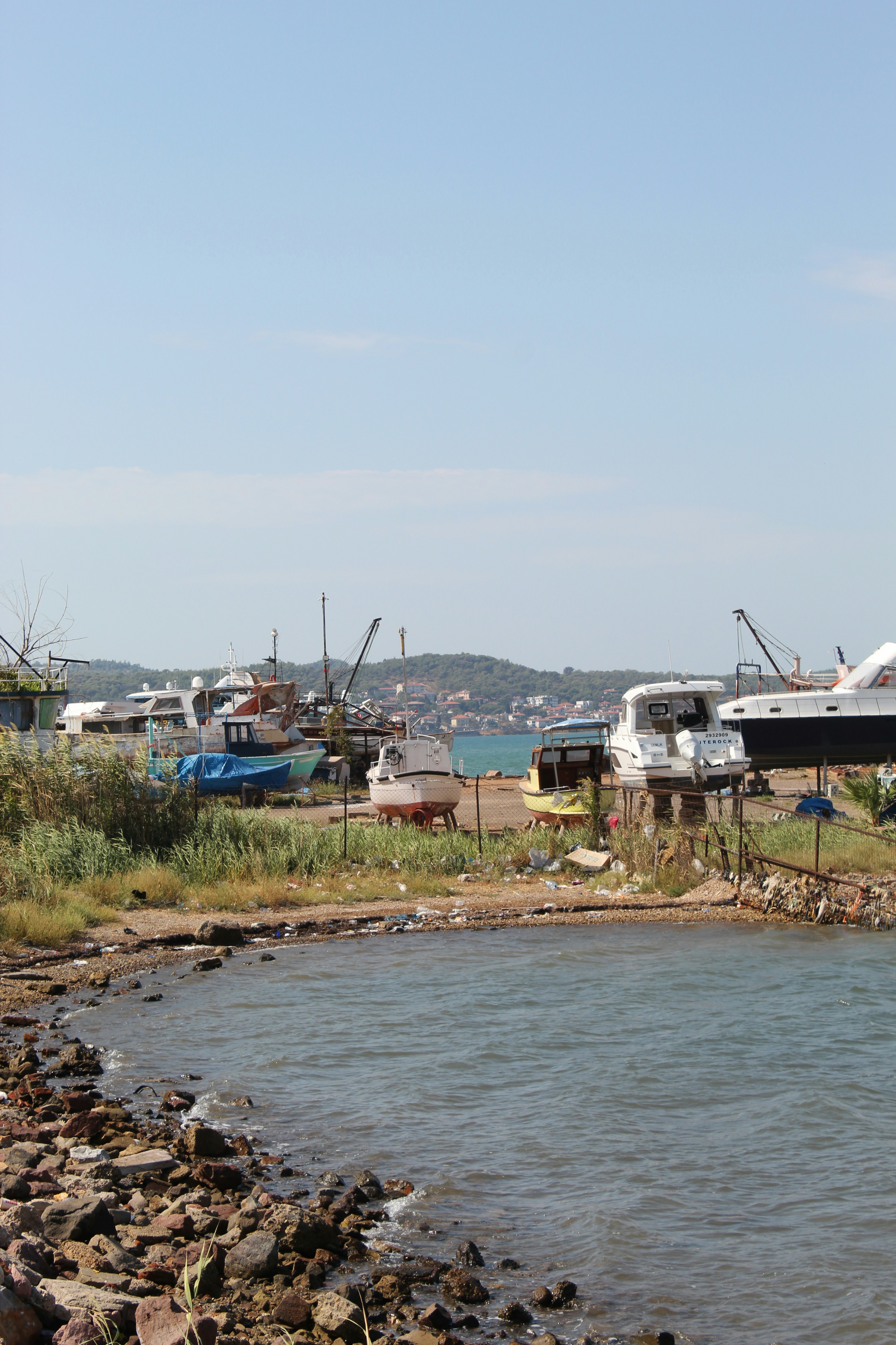 Boats on dry land near a rocky shoreline with a distant coastal town