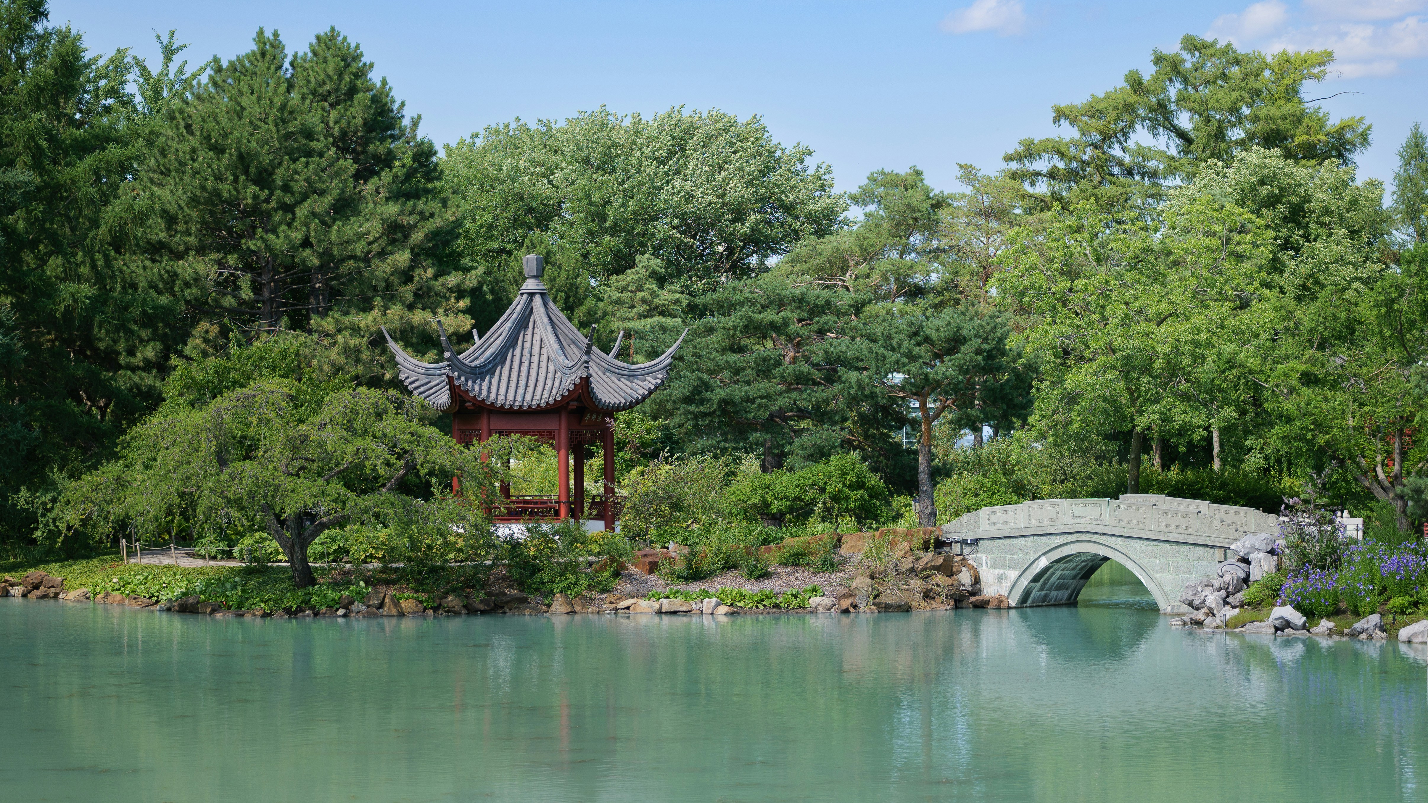 A traditional pagoda pavilion and stone bridge in a lush green garden