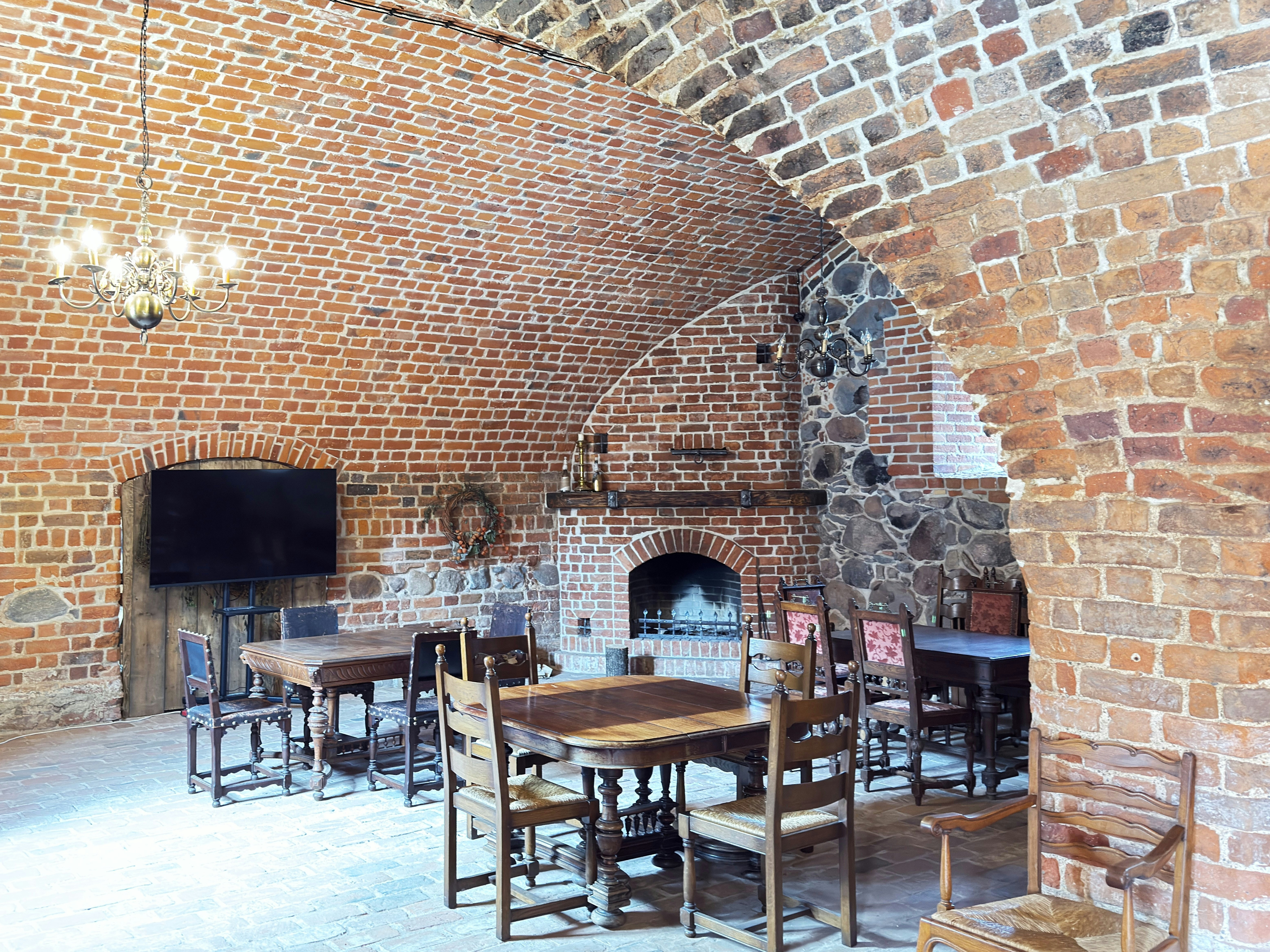 A rustic room with a vaulted brick ceiling, wooden tables, and a stone fireplace
