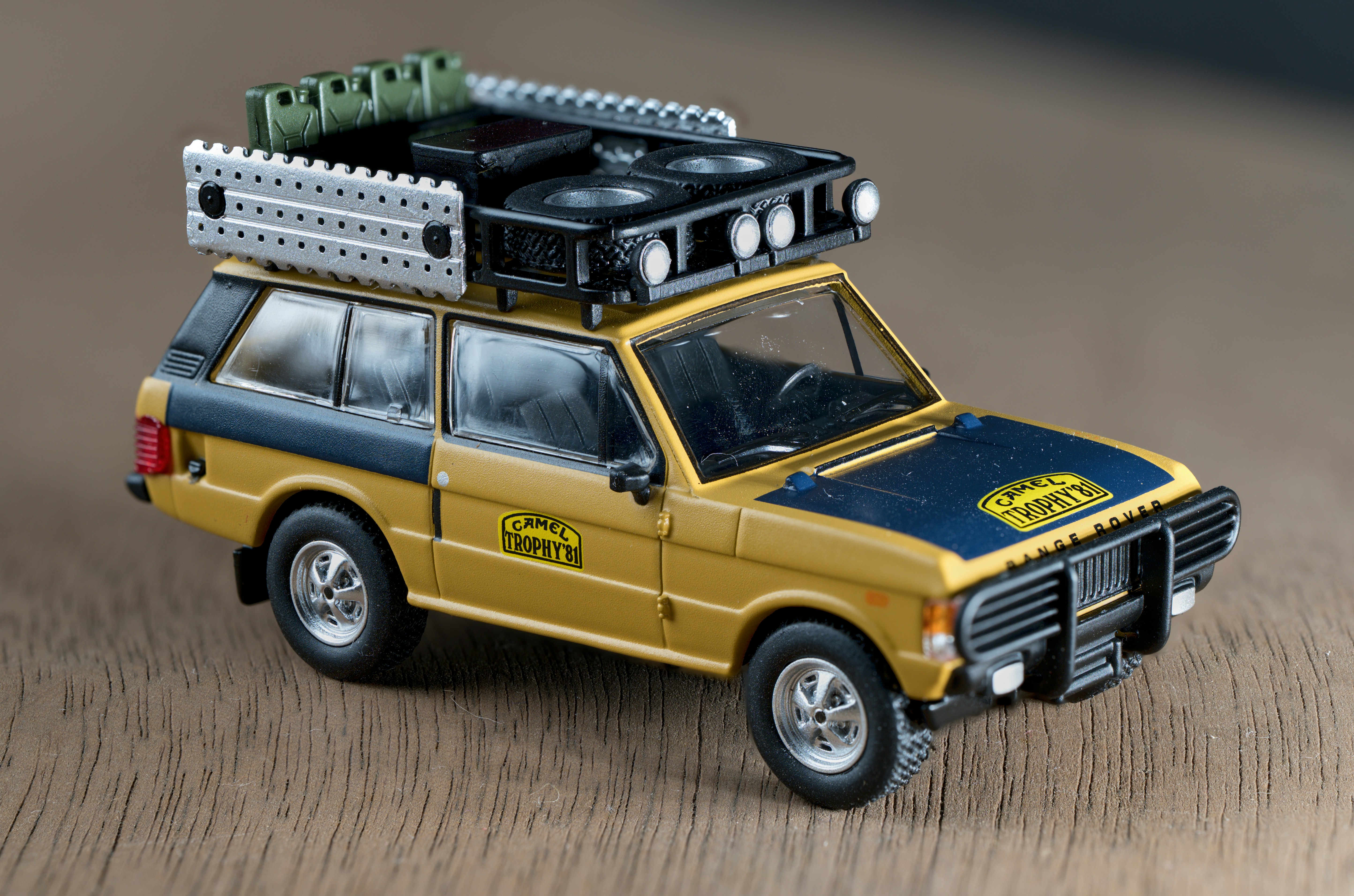 A yellow and blue toy Range Rover with roof rack gear on wood