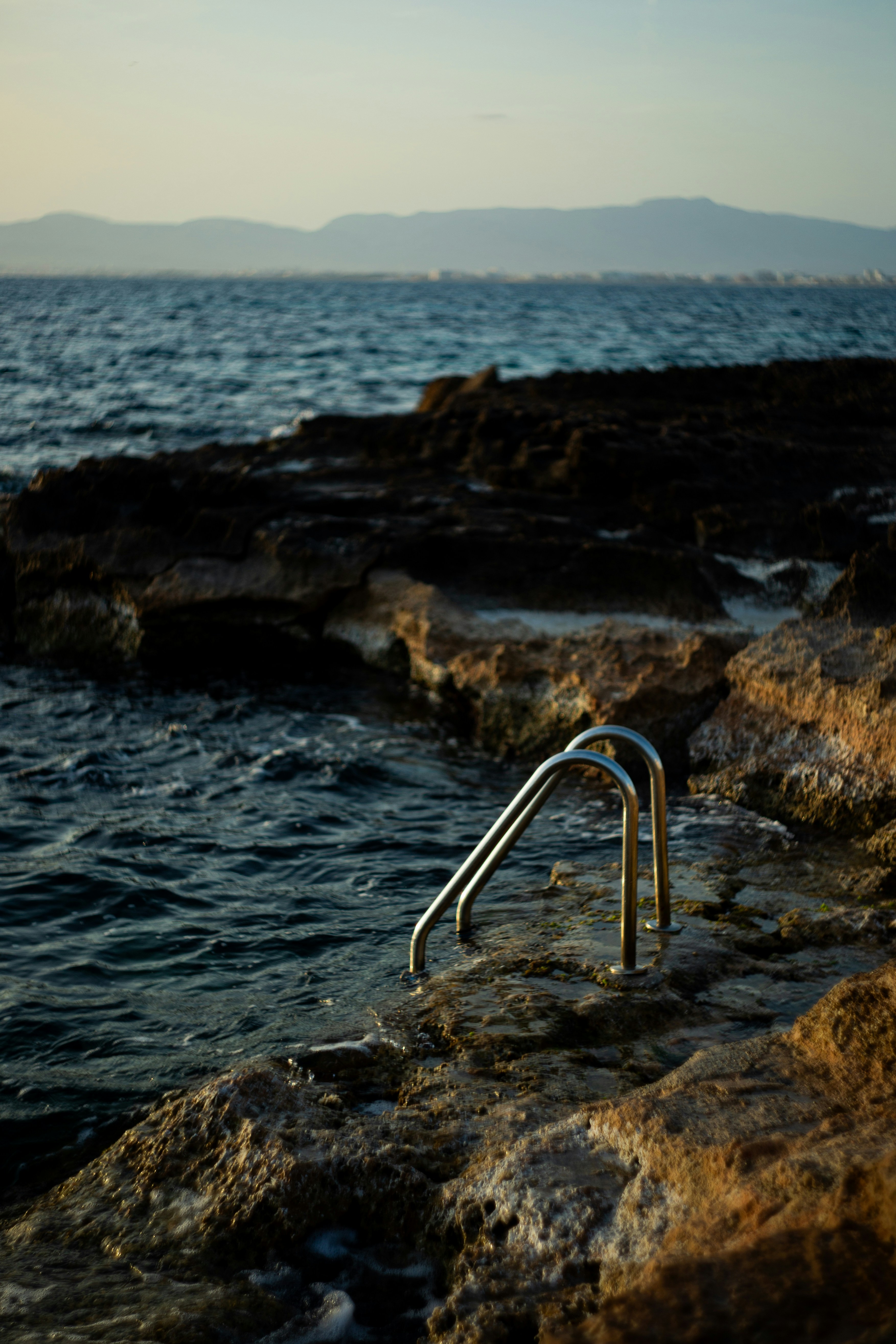 Metal pool ladder attached to a rocky coastline beside the dark blue sea