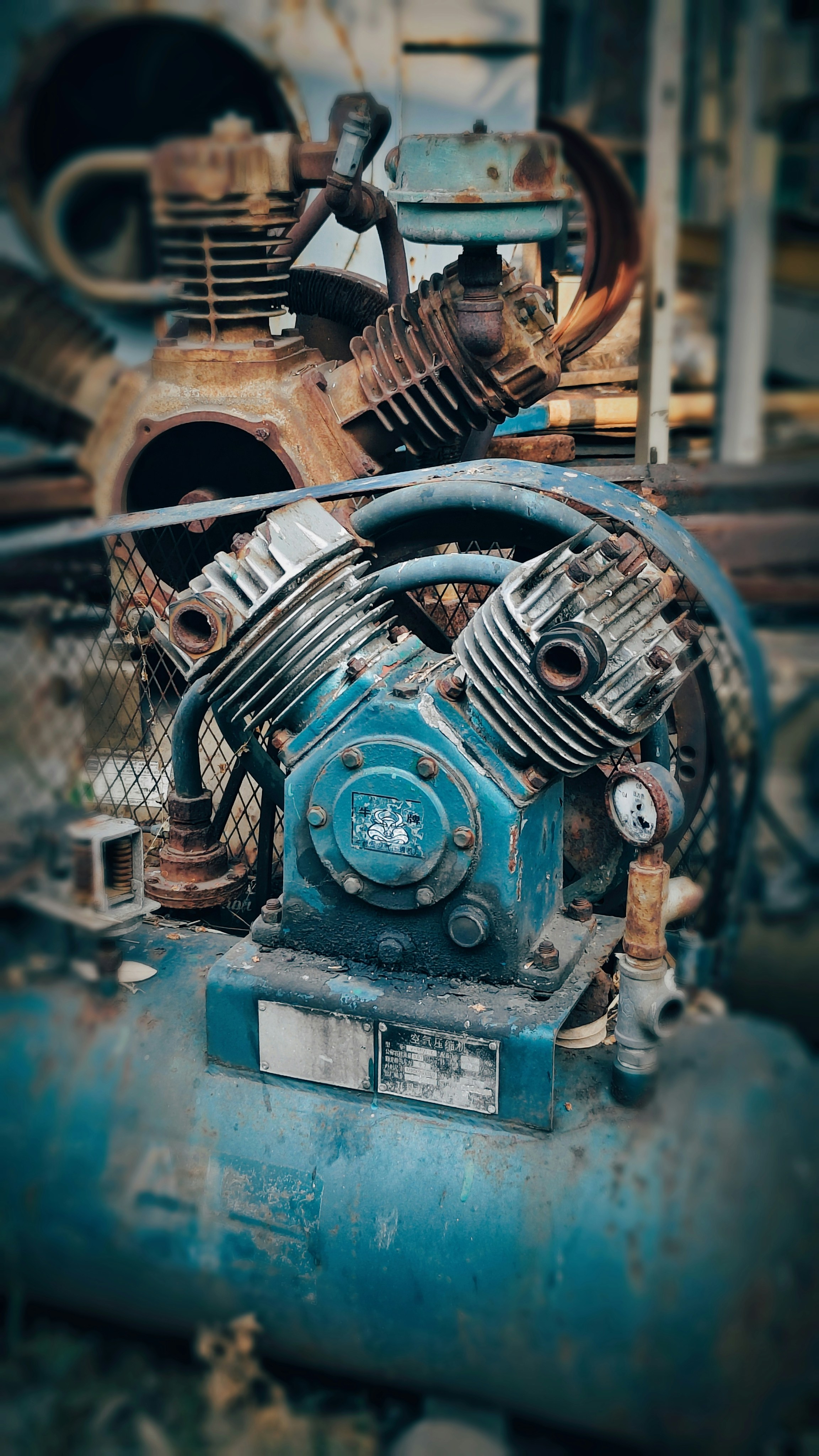 A weathered blue industrial air compressor with rusted metal components and a pressure gauge