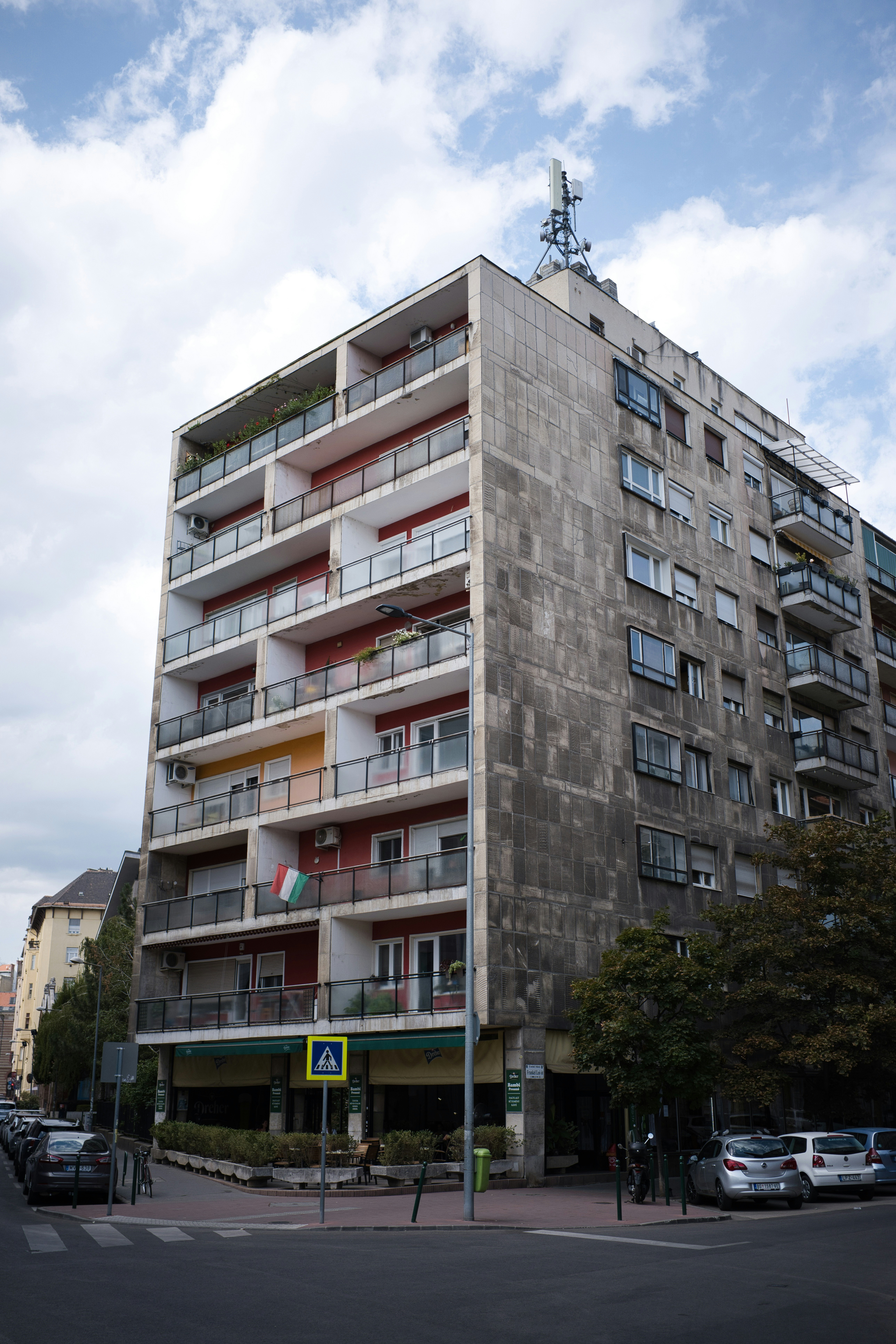 A tall apartment building with red balconies and a grey tiled facade