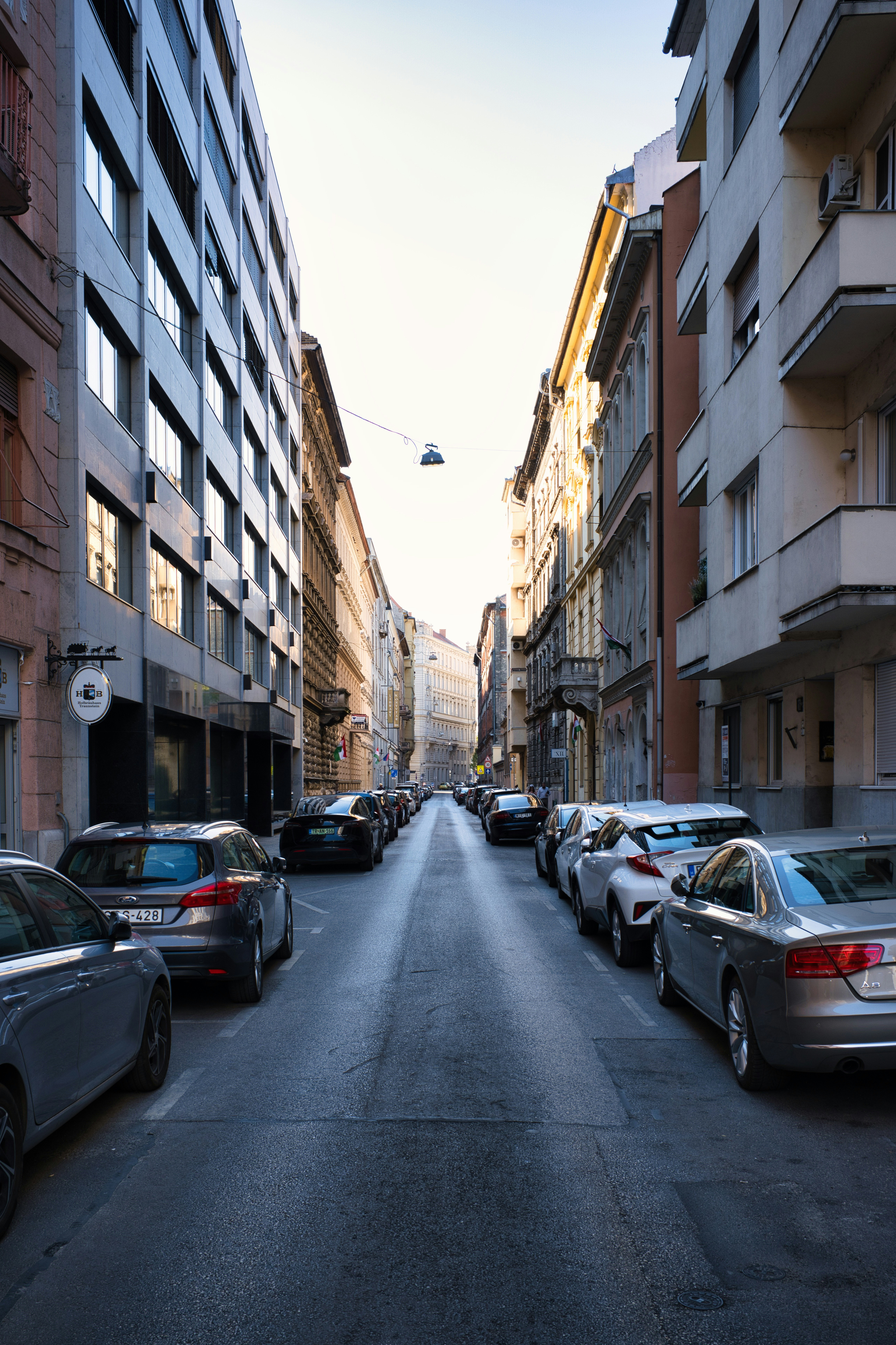 Cars parked along a narrow city street between tall apartment buildings