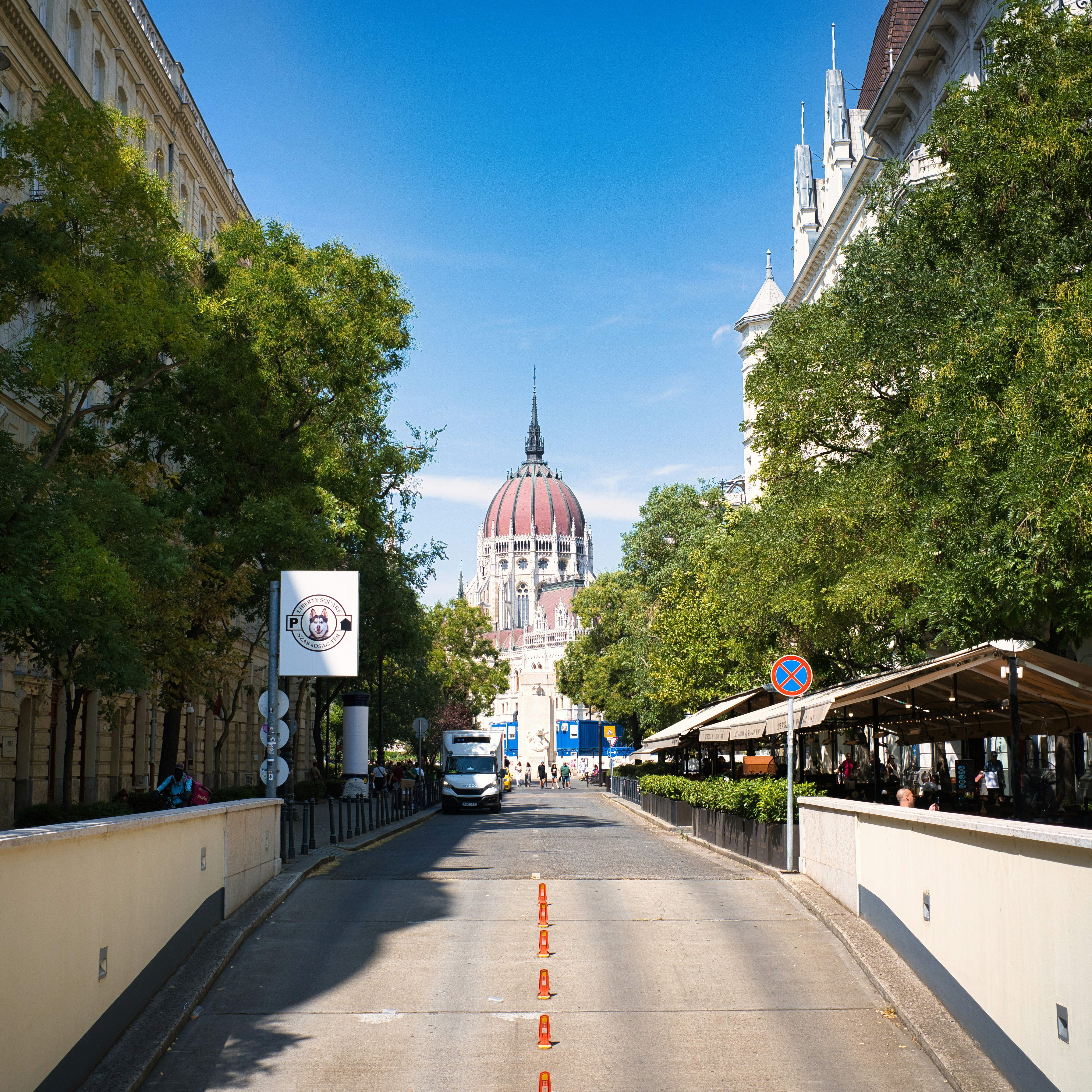 The Hungarian Parliament Building dome visible at the end of a tree-lined street in Budapest
