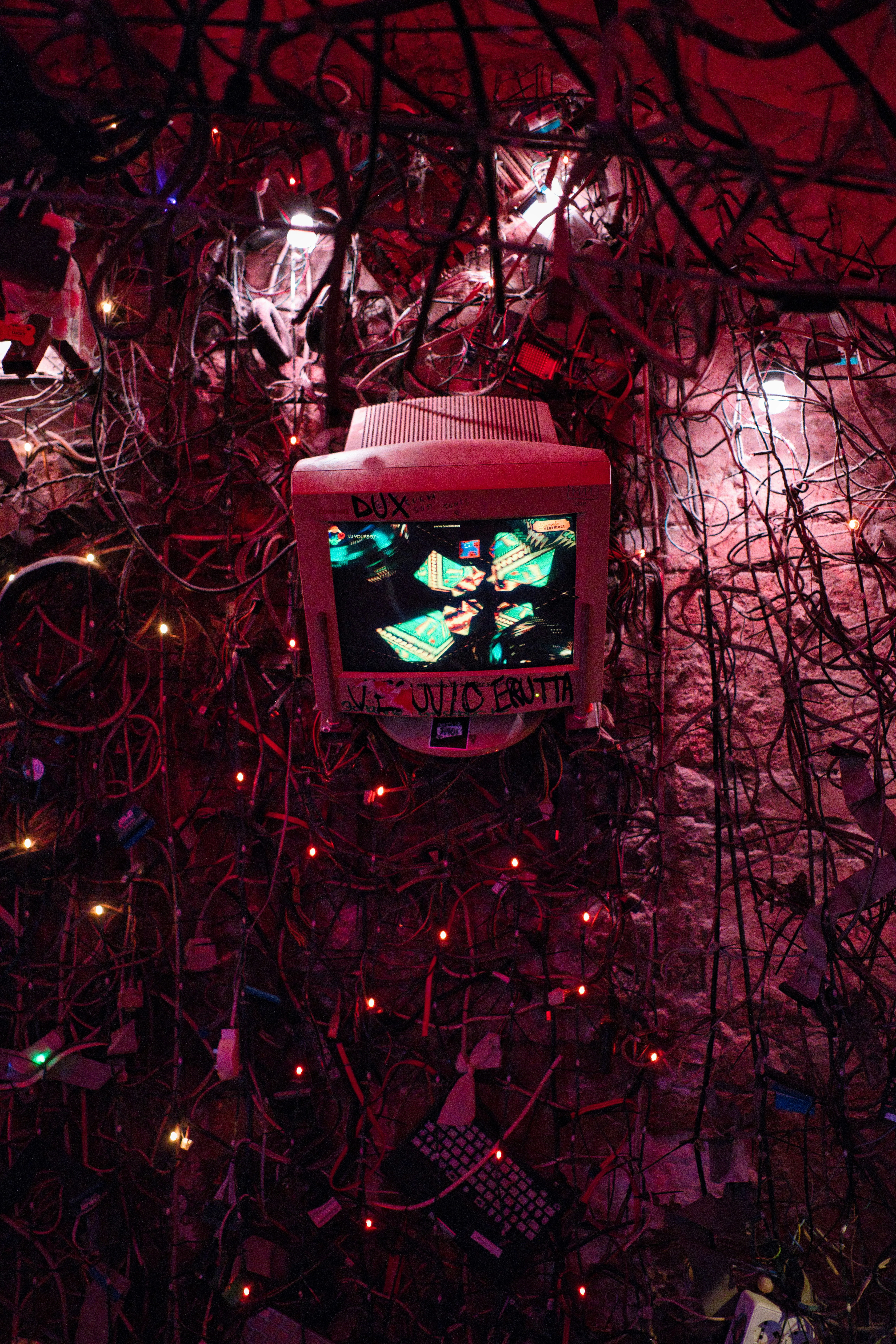 A vintage computer monitor surrounded by a dense tangle of black cables and lights