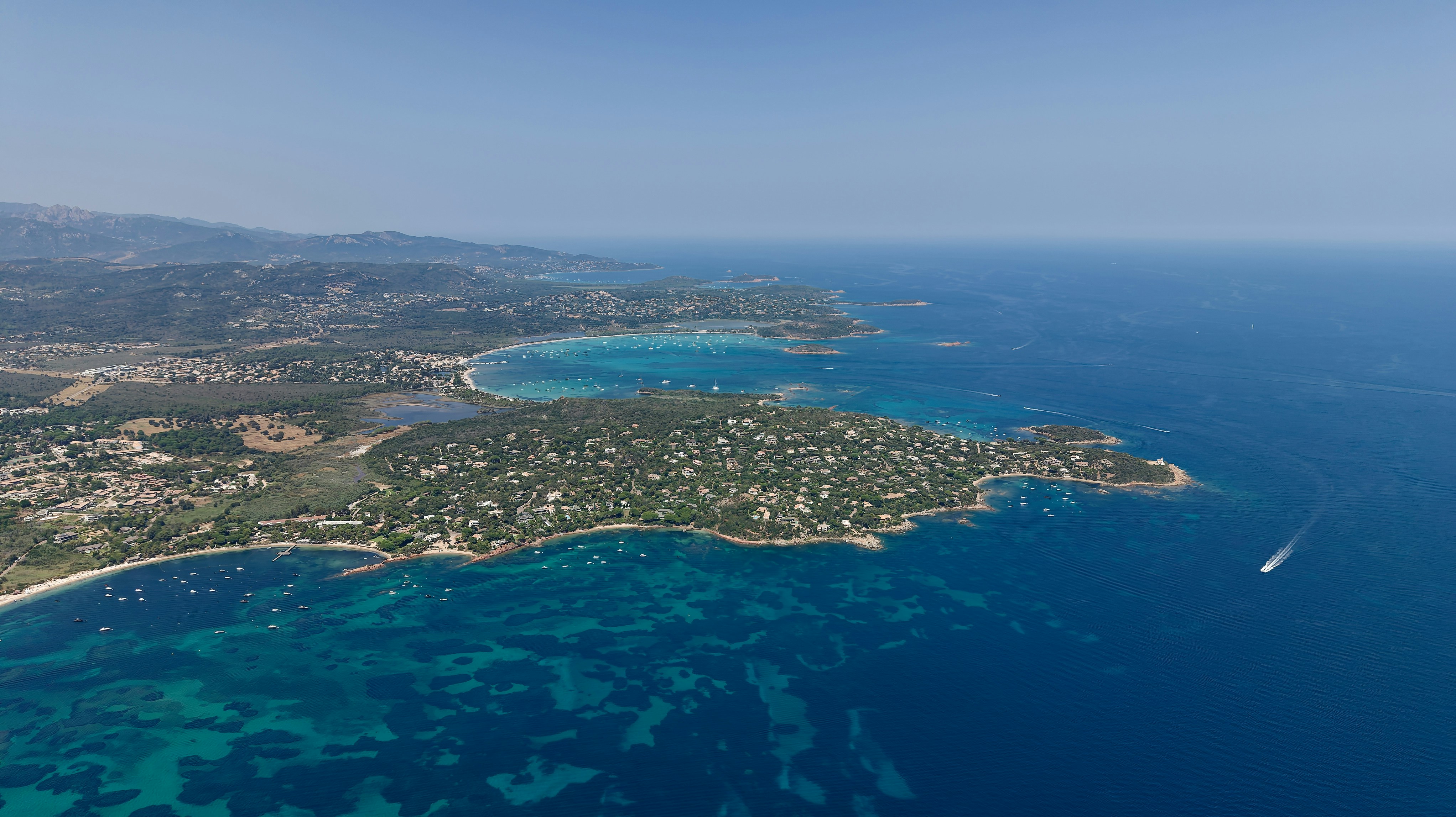 Aerial view of a Mediterranean coastline with turquoise bays and a forested peninsula
