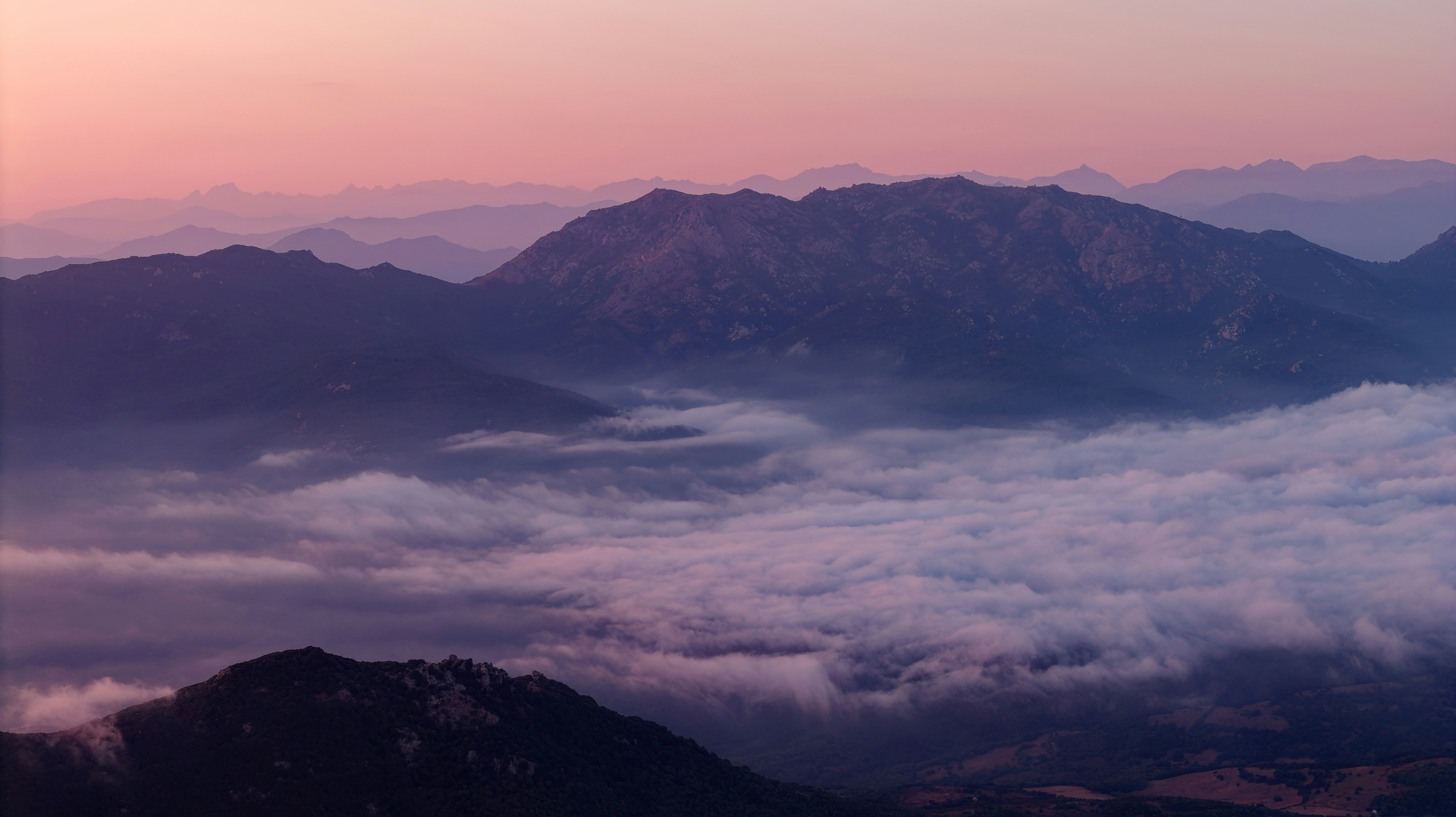 Layered mountain ridges rising above a thick blanket of low clouds at golden hour