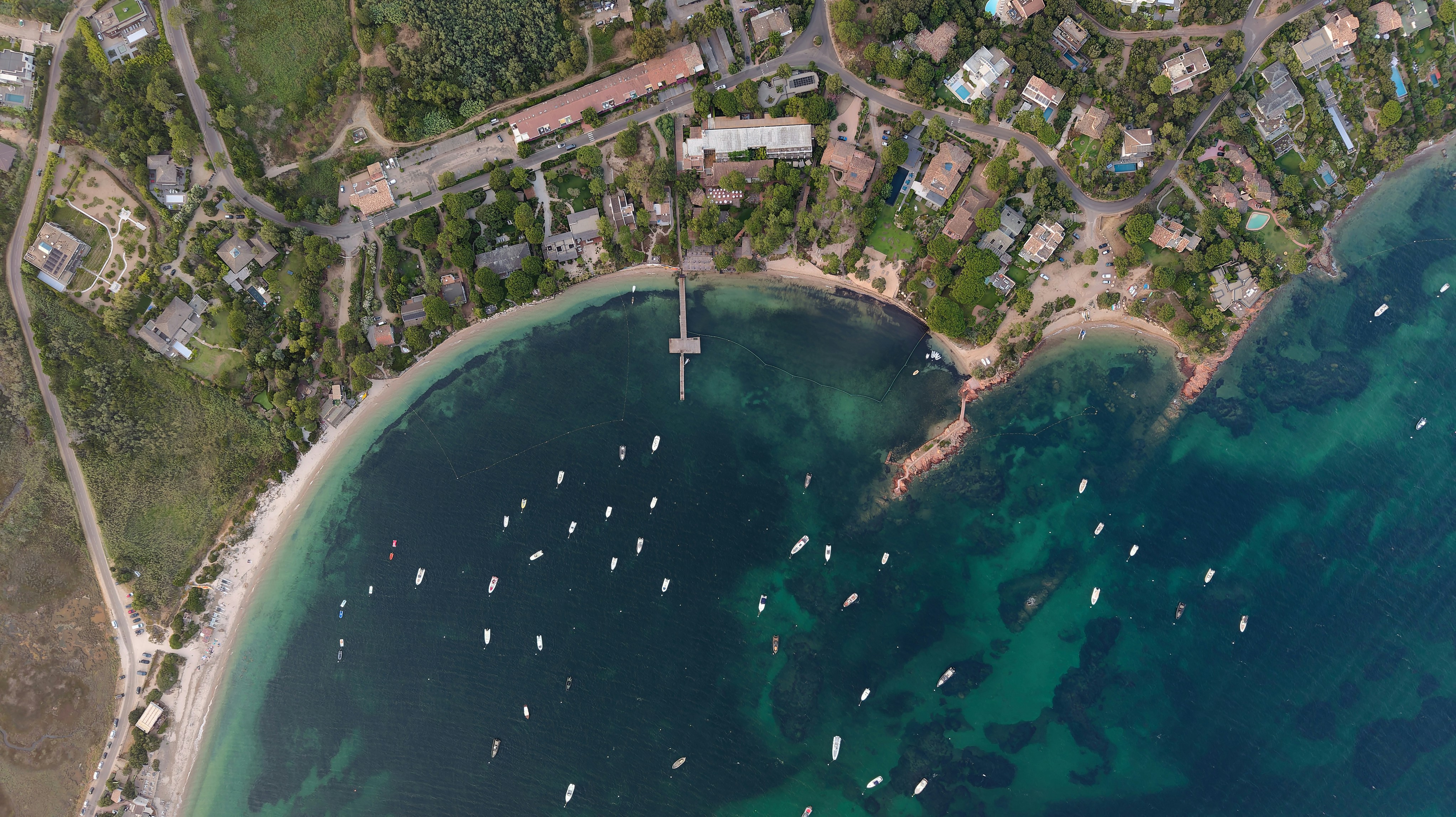 An aerial view of a coastal bay with boats anchored near a wooden pier