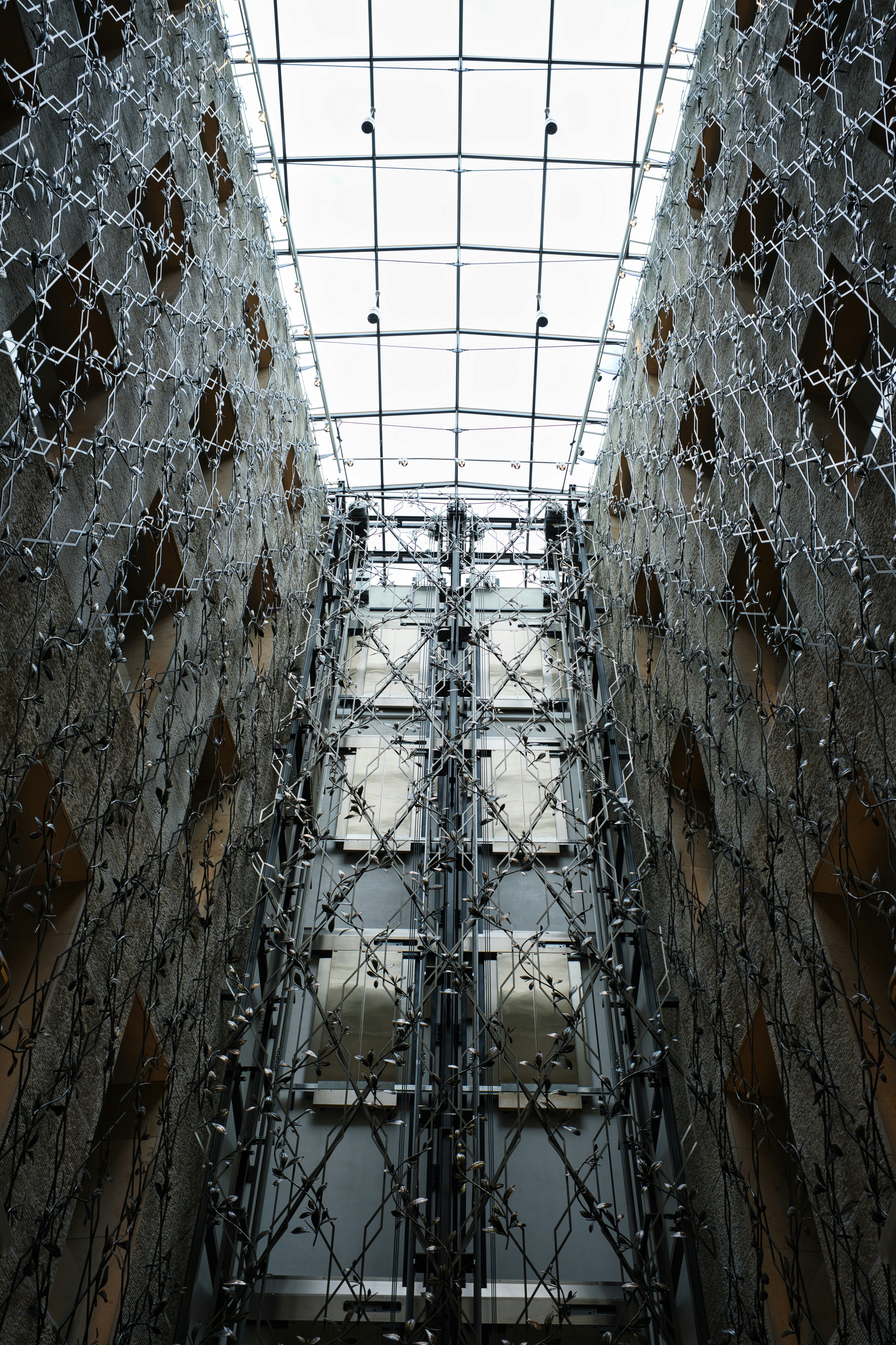 A glass atrium with metal vine sculptures climbing the textured stone walls