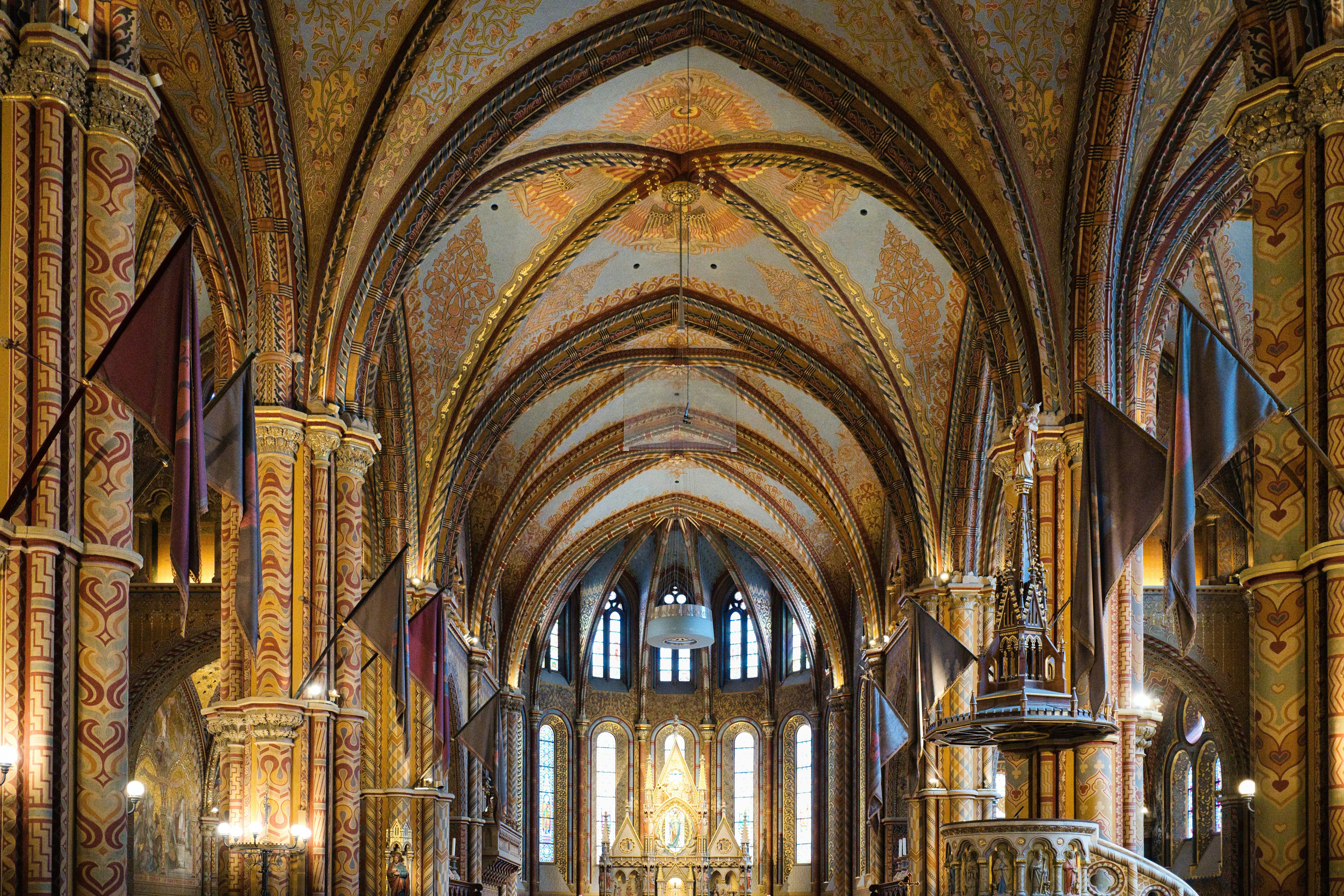 The ornate vaulted ceiling and interior of Matthias Church in Budapest with hanging flags