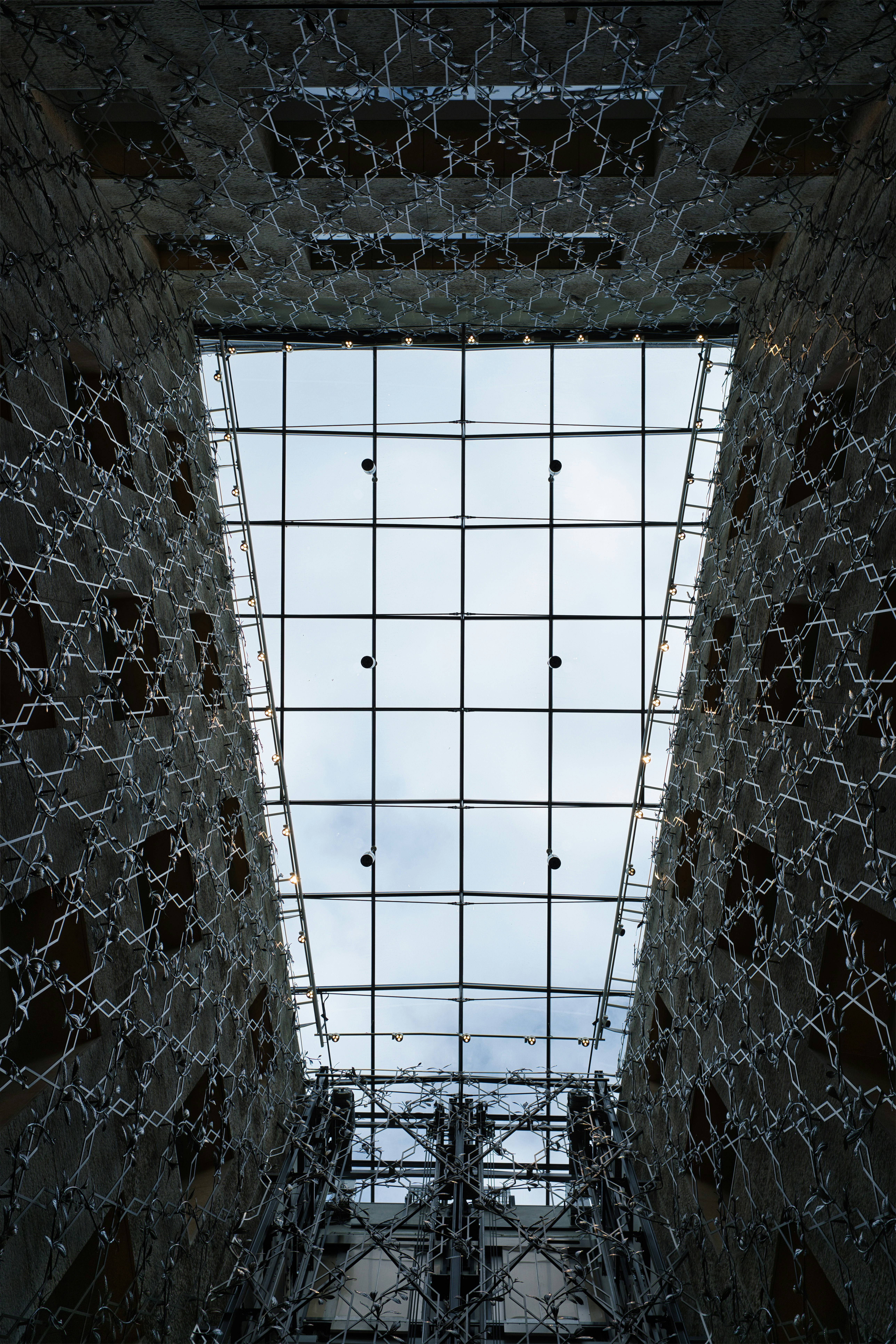 A glass atrium ceiling framed by walls with intricate metal lattice patterns