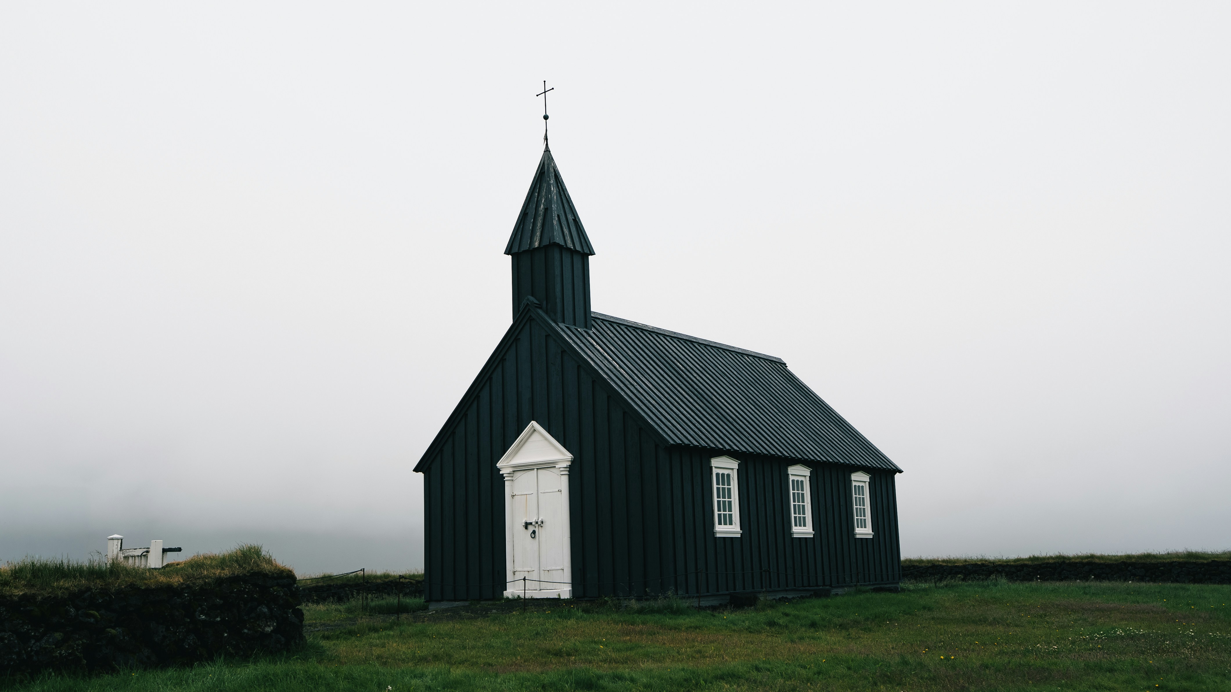 A black wooden church with white doors in a misty field in Iceland