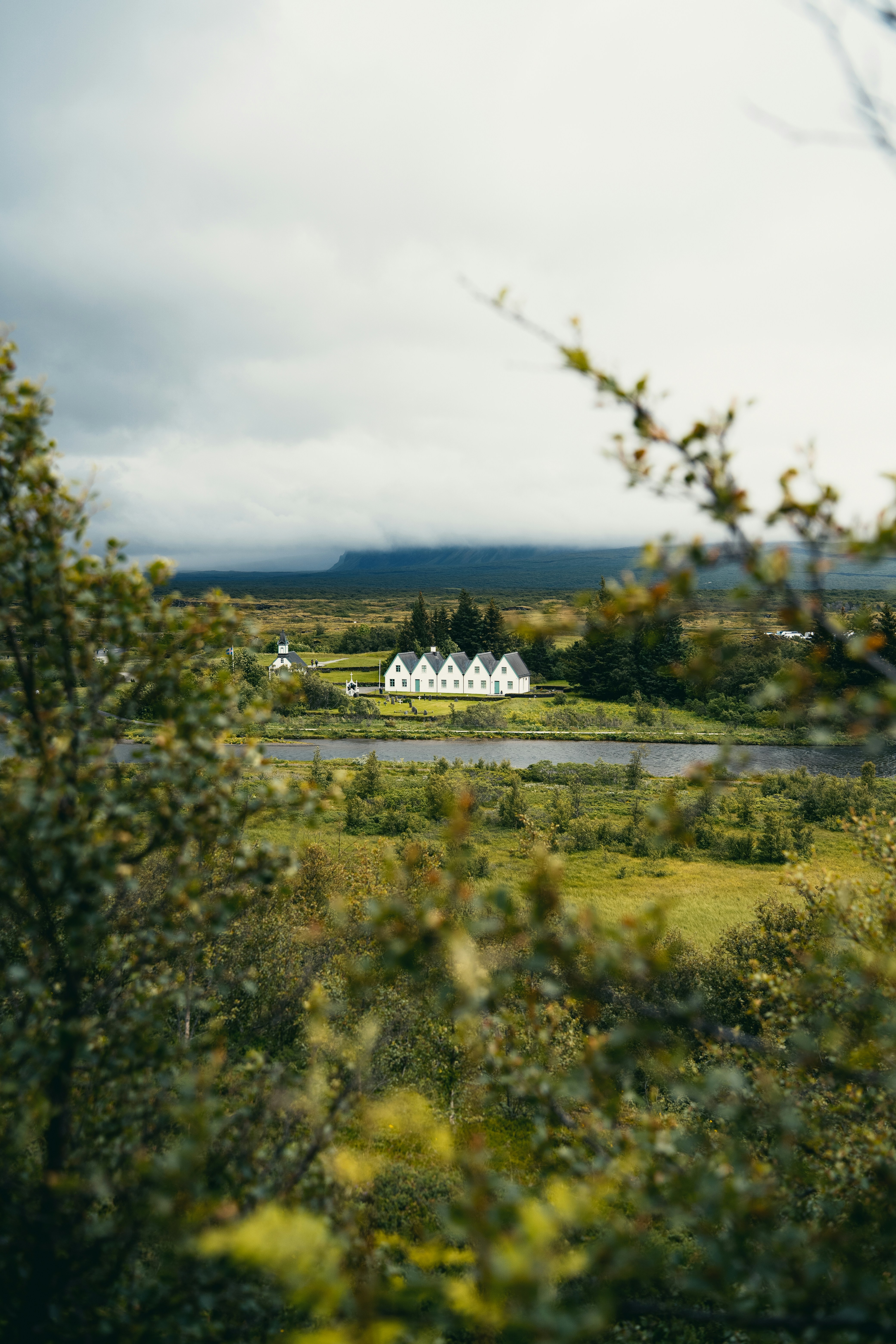 A white house with multiple gables in a green valley under cloudy skies