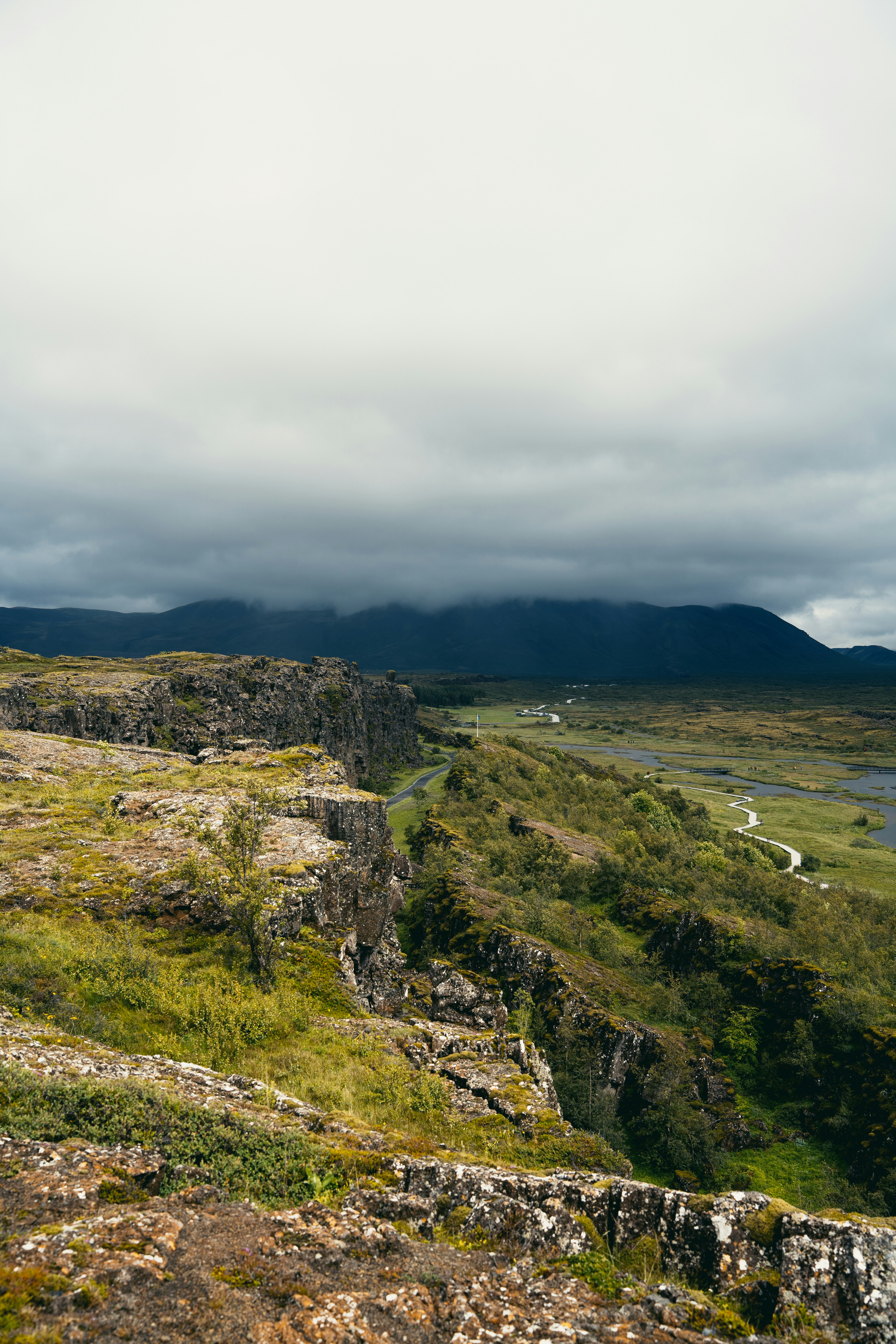 Rugged mossy cliffs overlooking a green valley with a winding path in Iceland
