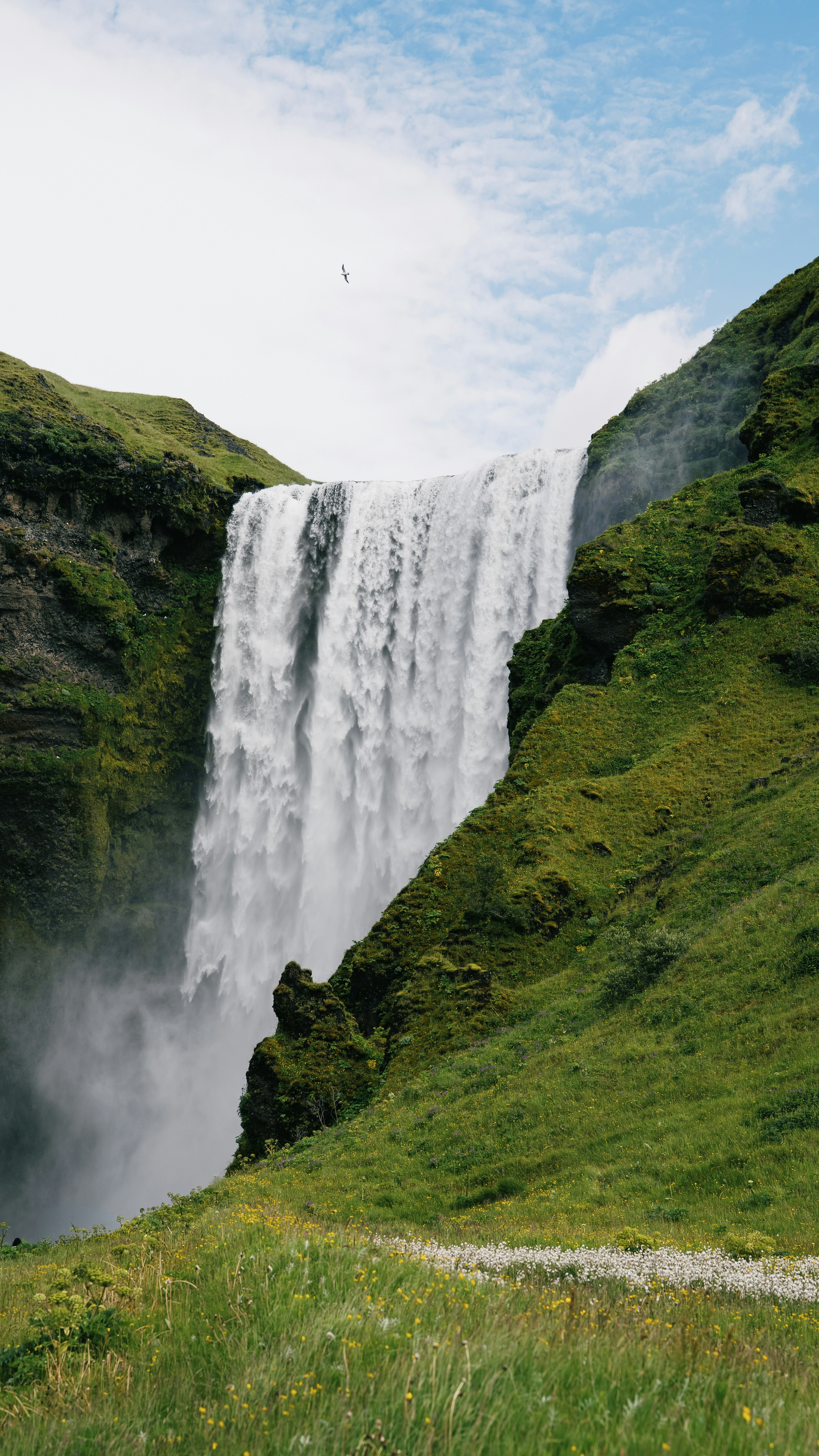 A large waterfall cascading down a green cliff into a misty basin