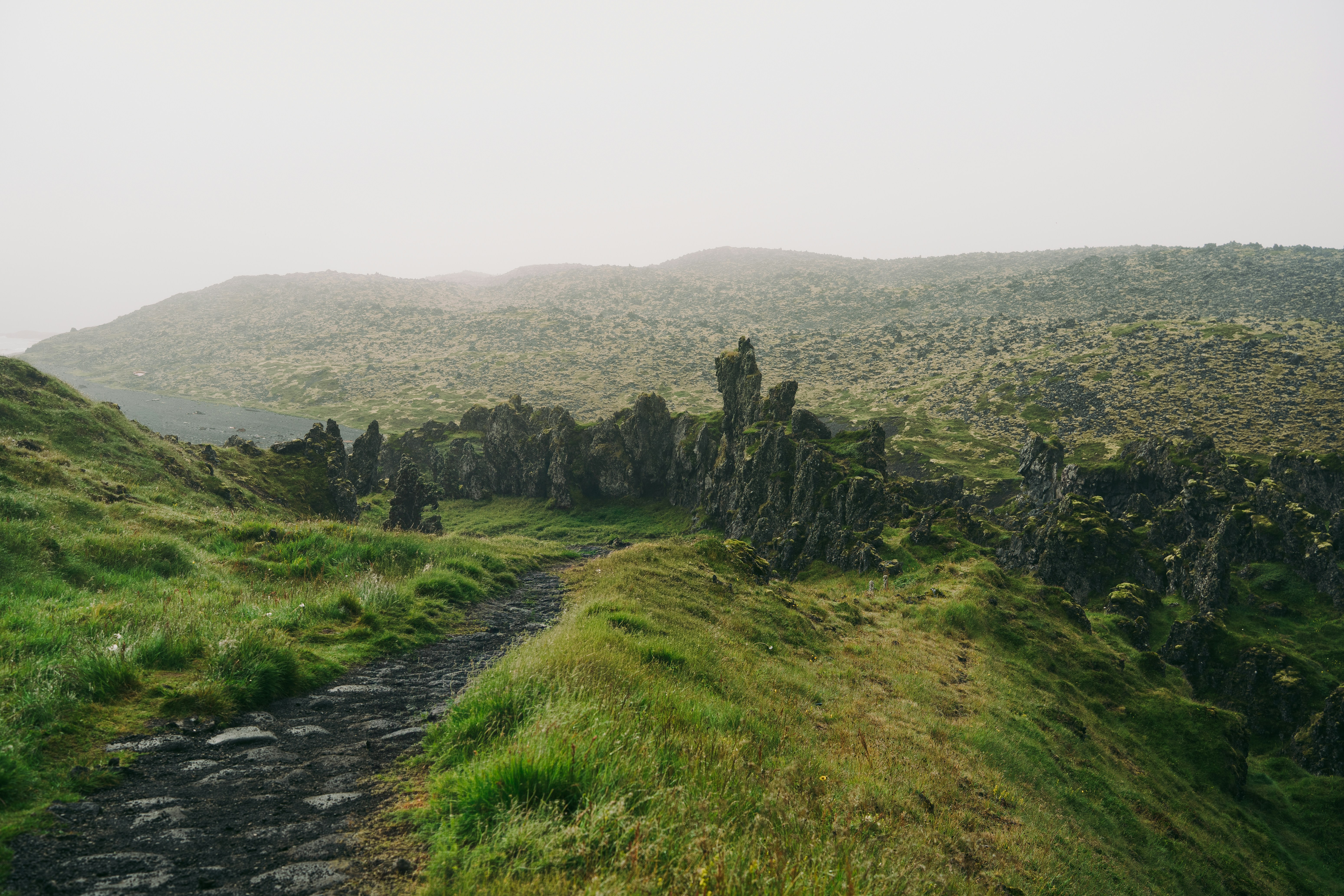 A narrow dirt path winding through mossy green hills and jagged volcanic rock formations