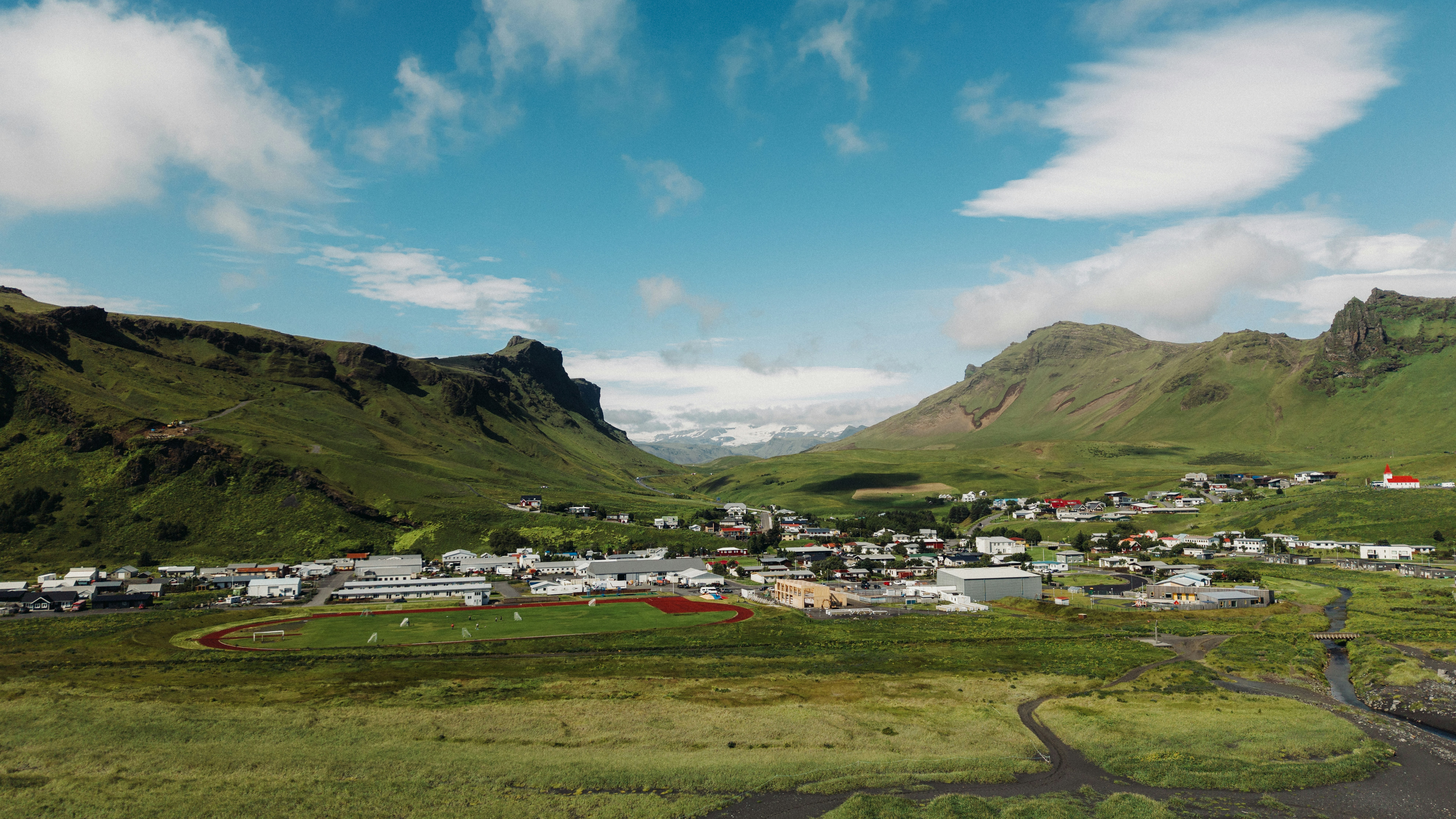 A small town nestled in a green valley between steep mountains under a blue sky