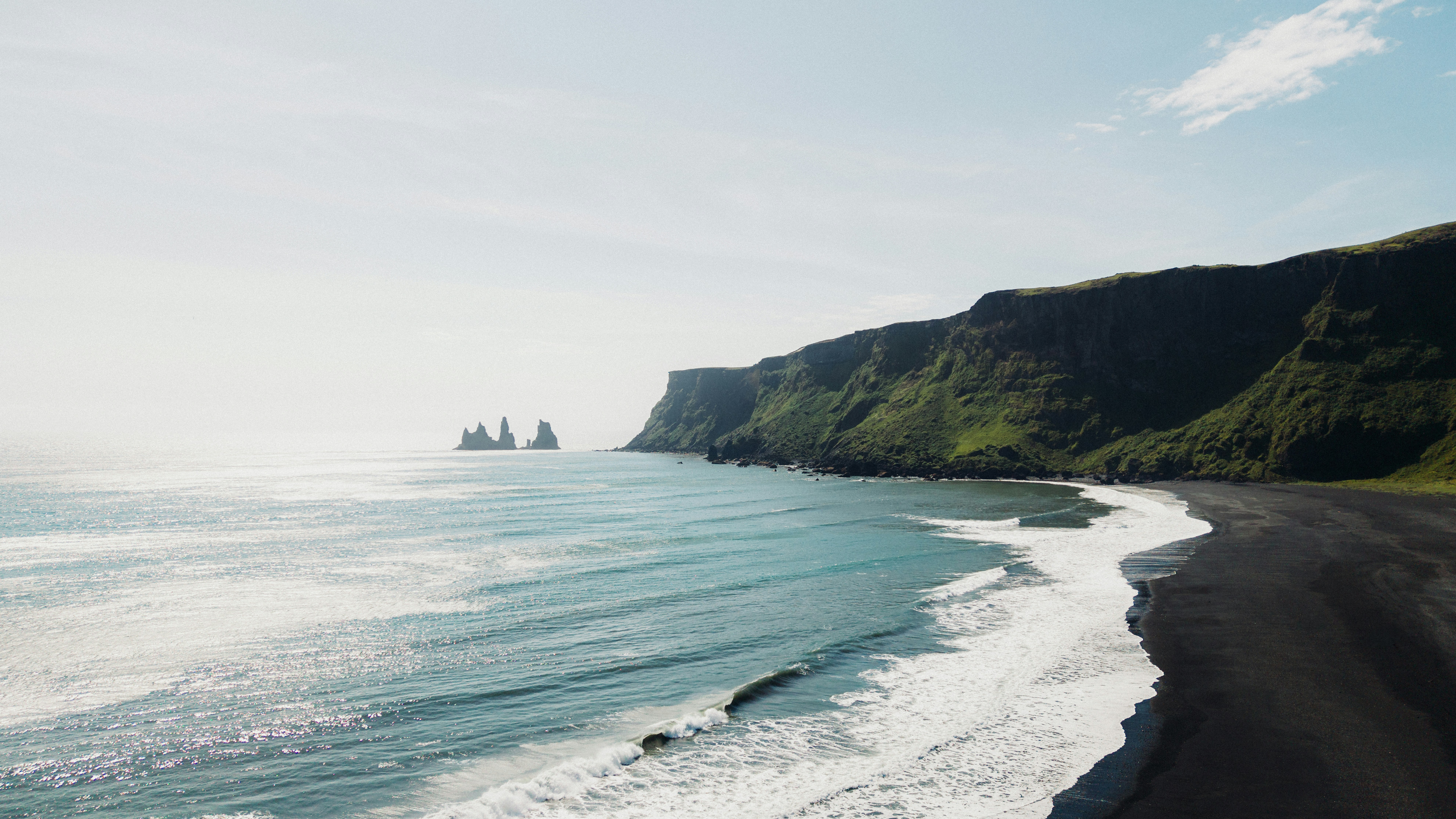 A black sand beach with white waves and green cliffs in Reynisfjara, Iceland