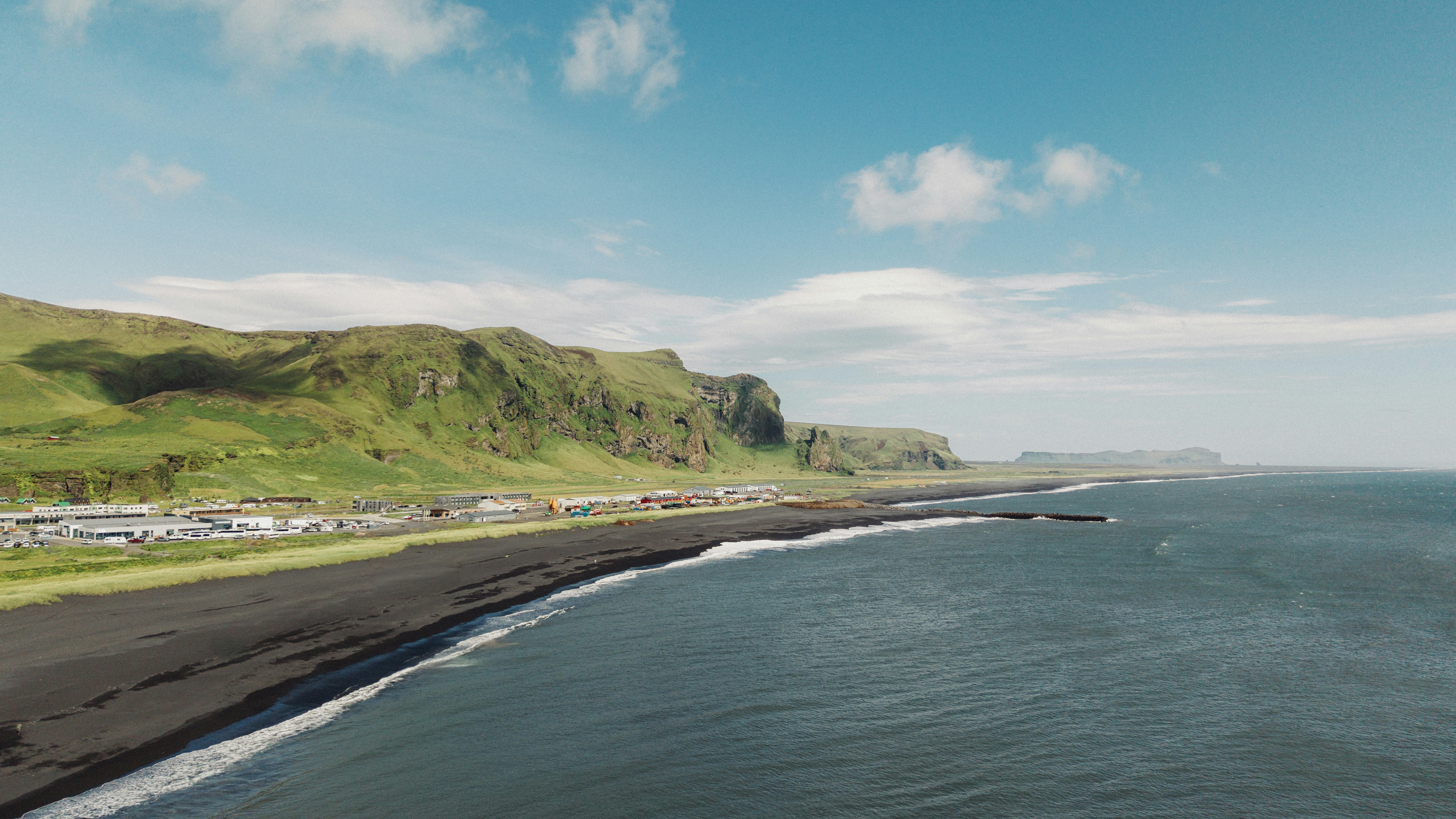 A black sand beach below green cliffs and a small town in Iceland