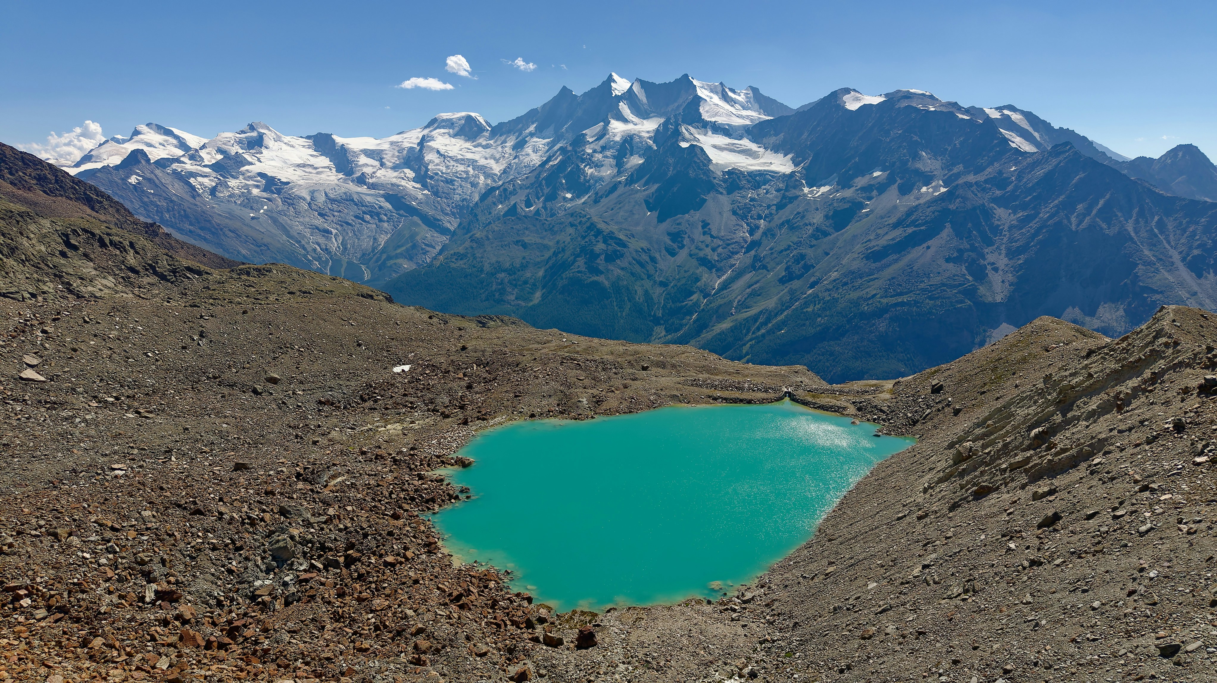 A turquoise glacial lake in a rocky mountain basin below snow-capped peaks