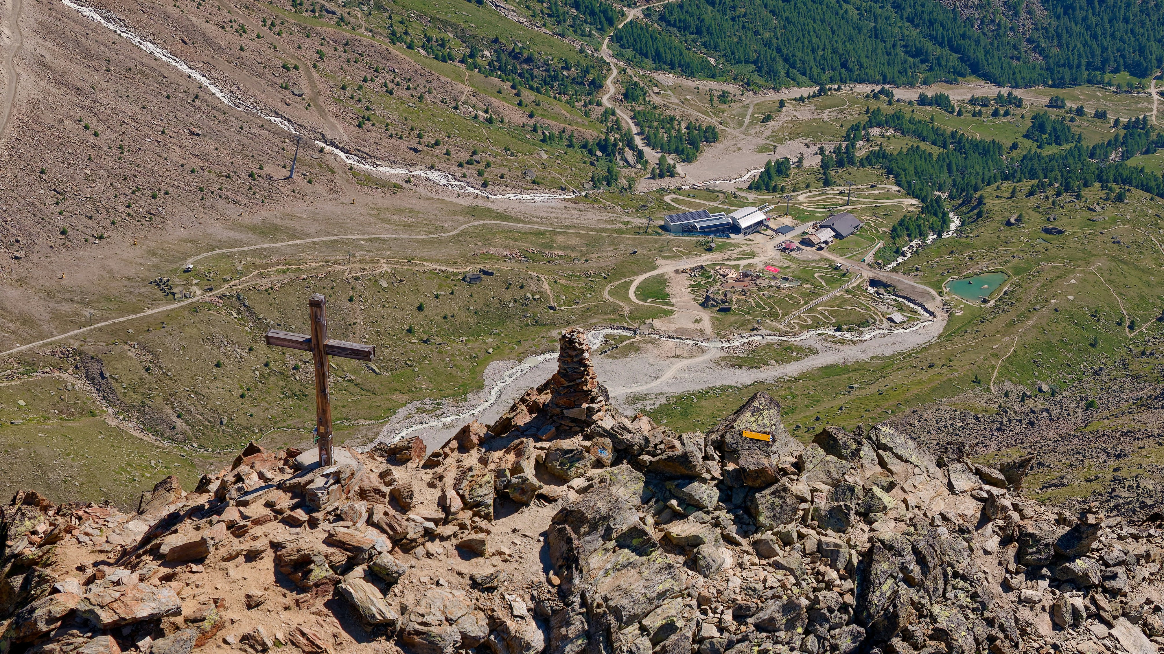 A wooden cross and stone cairn on a rocky mountain summit overlooking a valley