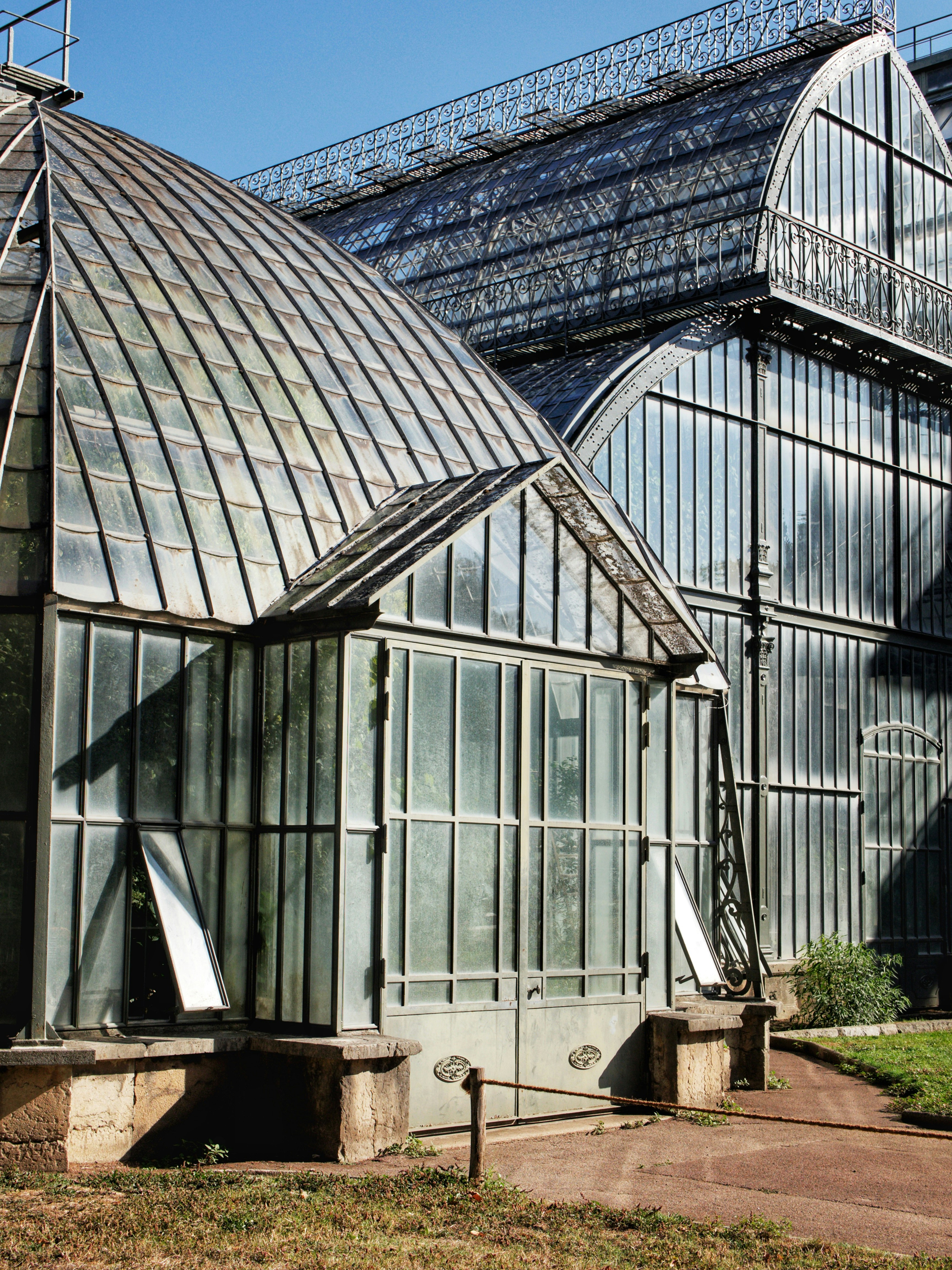 Ein viktorianisches Glasgewächshaus mit gewölbten Dächern und Metallrahmen in einem Garten