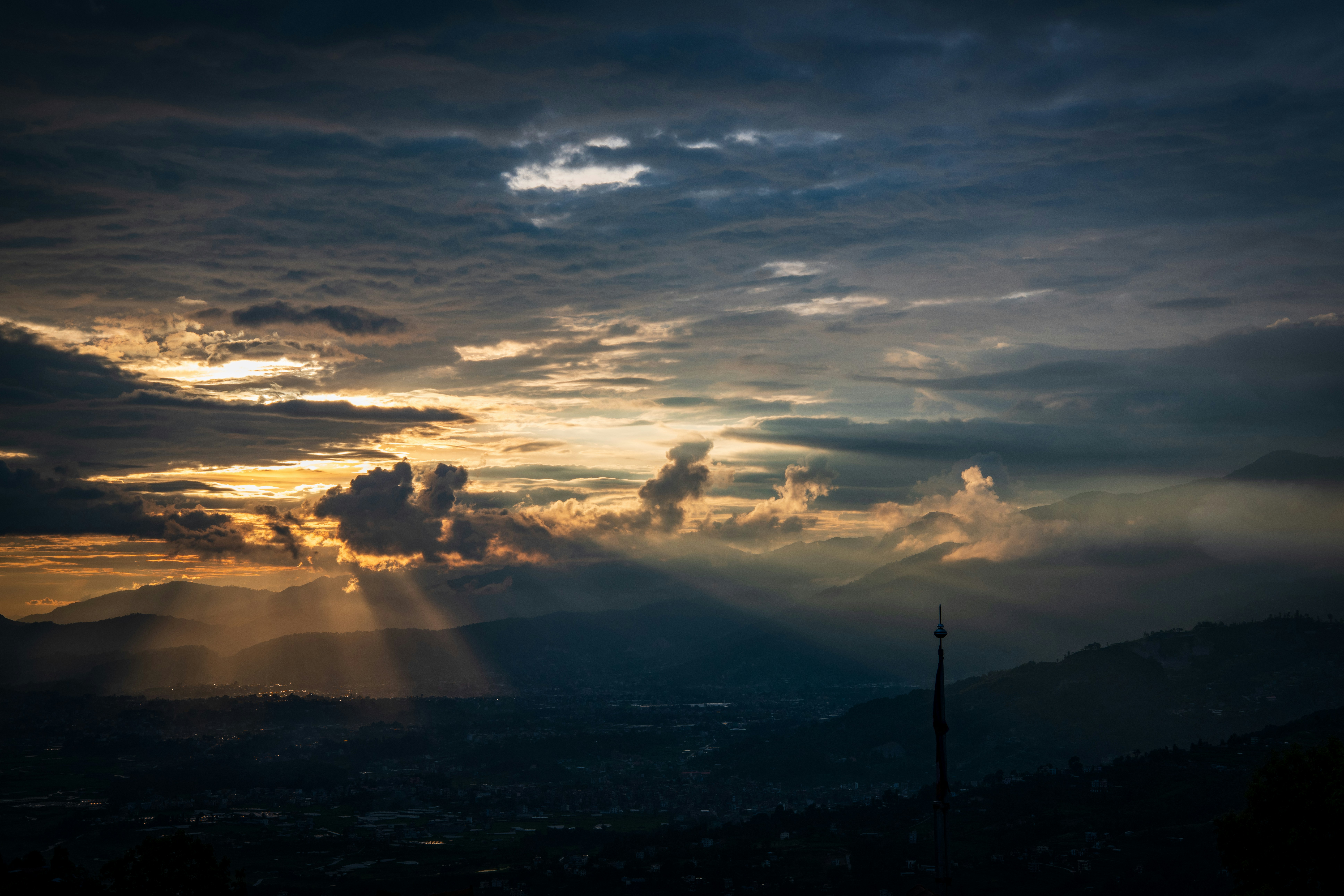 Sonnenlicht, das durch Wolken über ein dunkles Bergtal bei niedriger Sonne fällt.