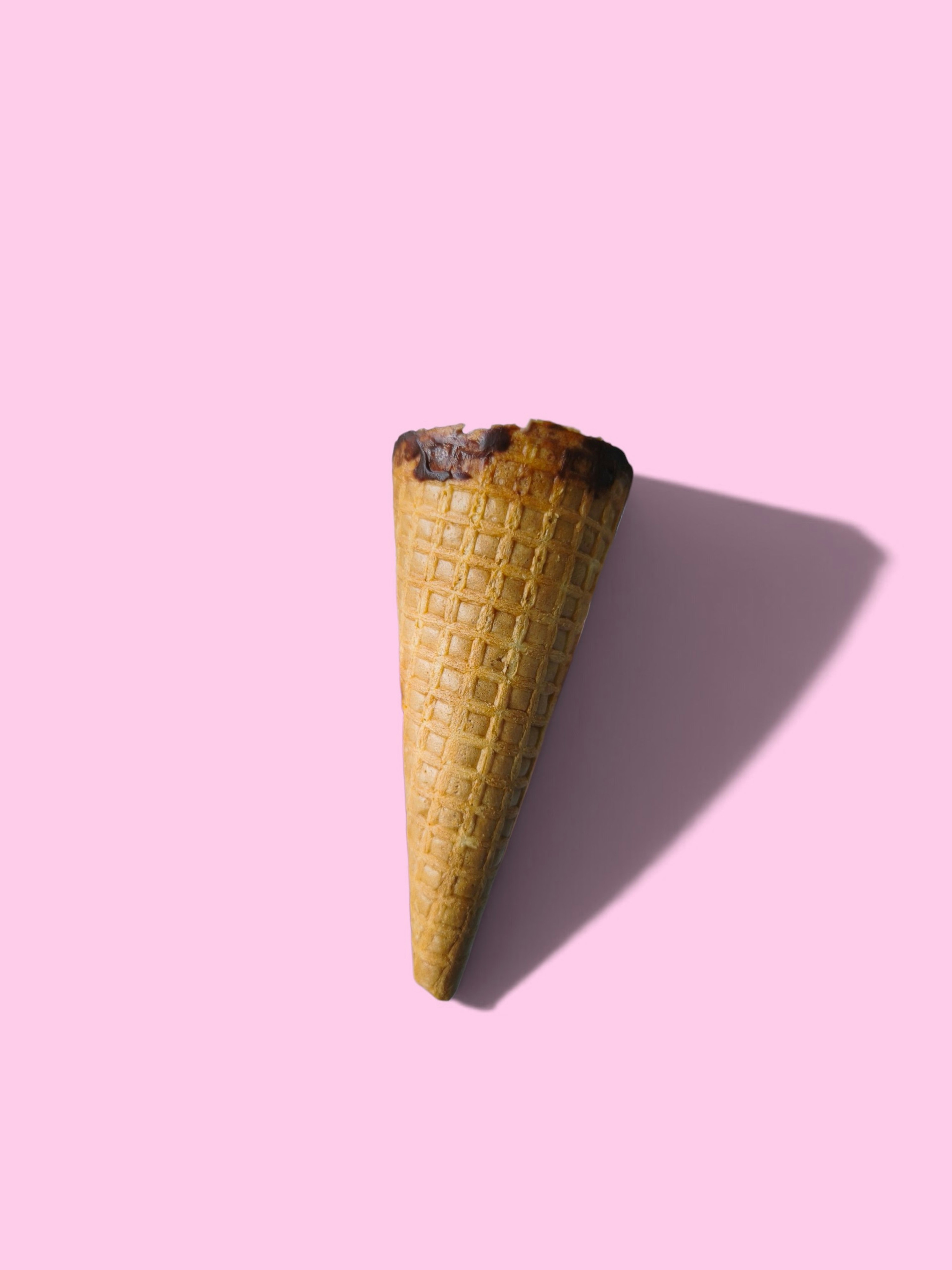 An empty waffle ice cream cone on a solid light pink background