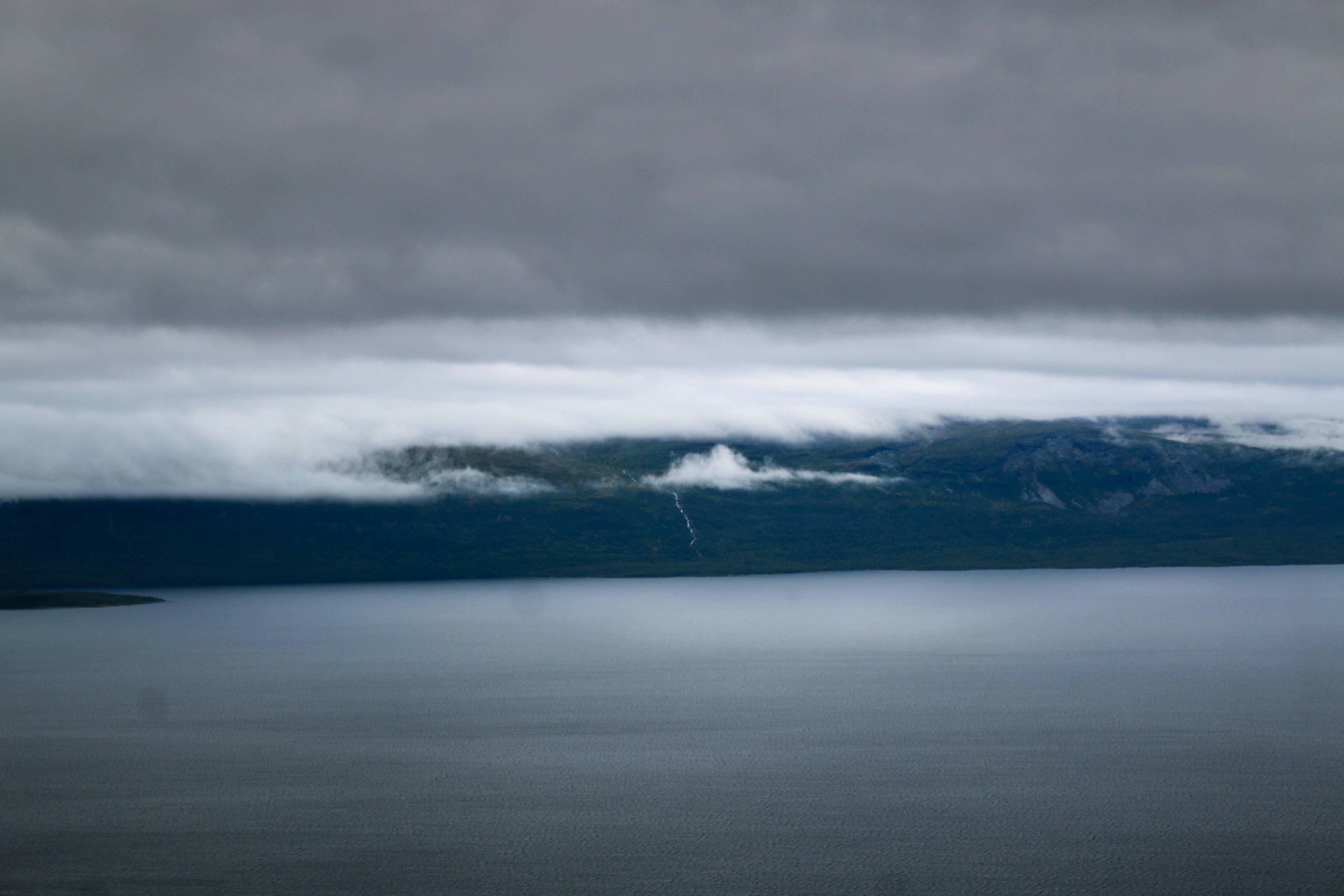 A dark lake beneath a low mountain range under heavy grey clouds