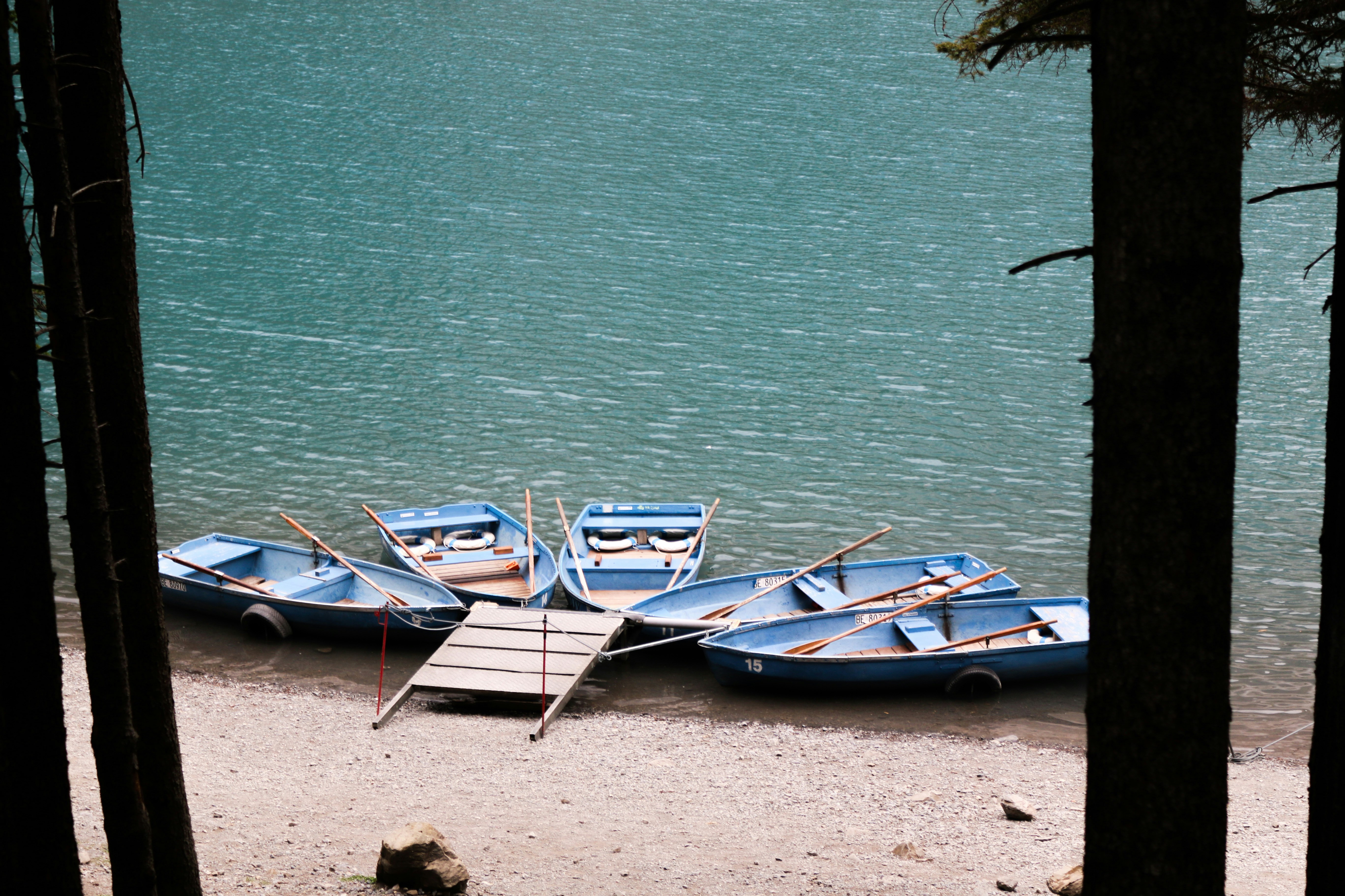 Five blue rowboats moored at a small wooden dock on a turquoise lake