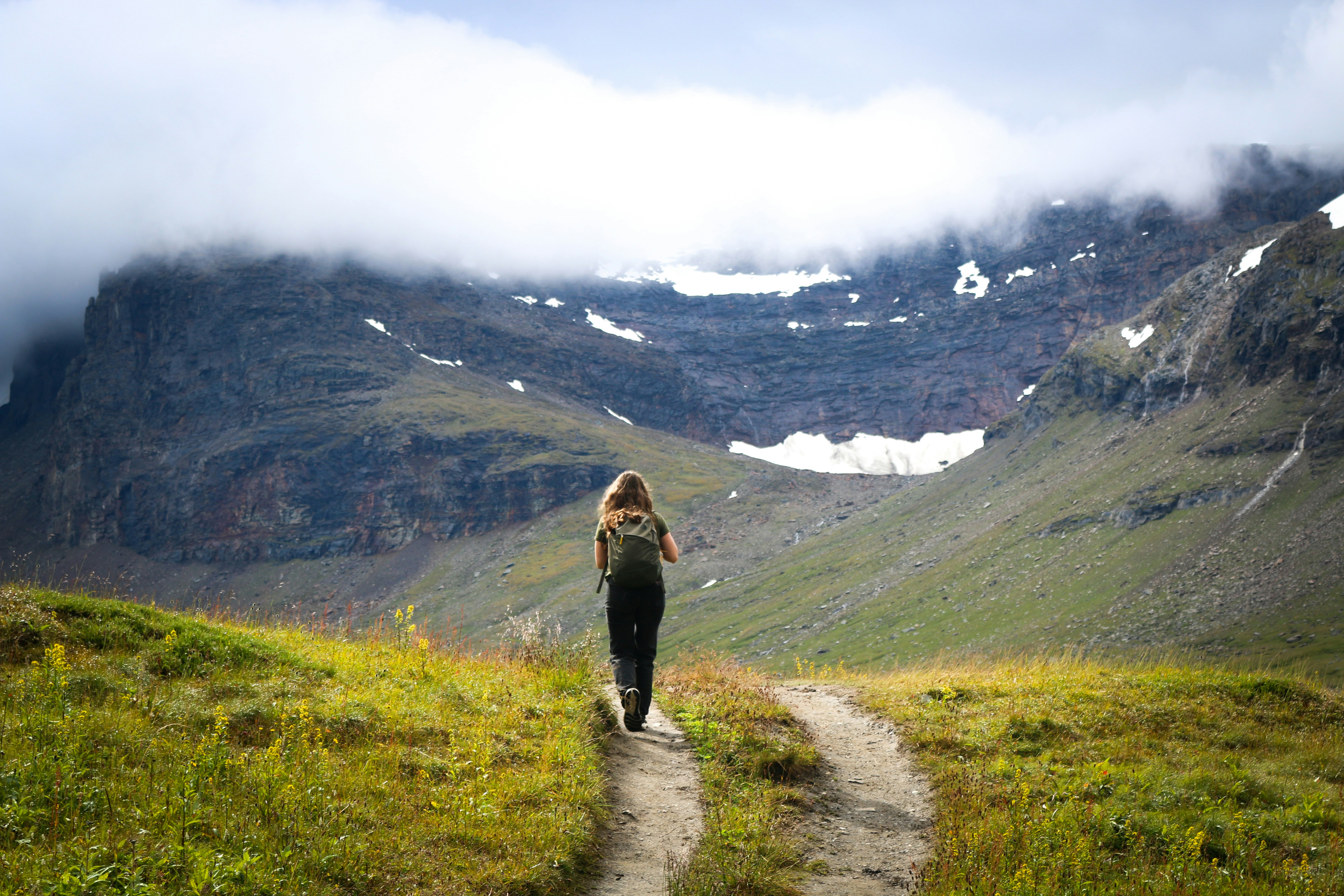 A person with a backpack walking along a dirt path toward a mountain