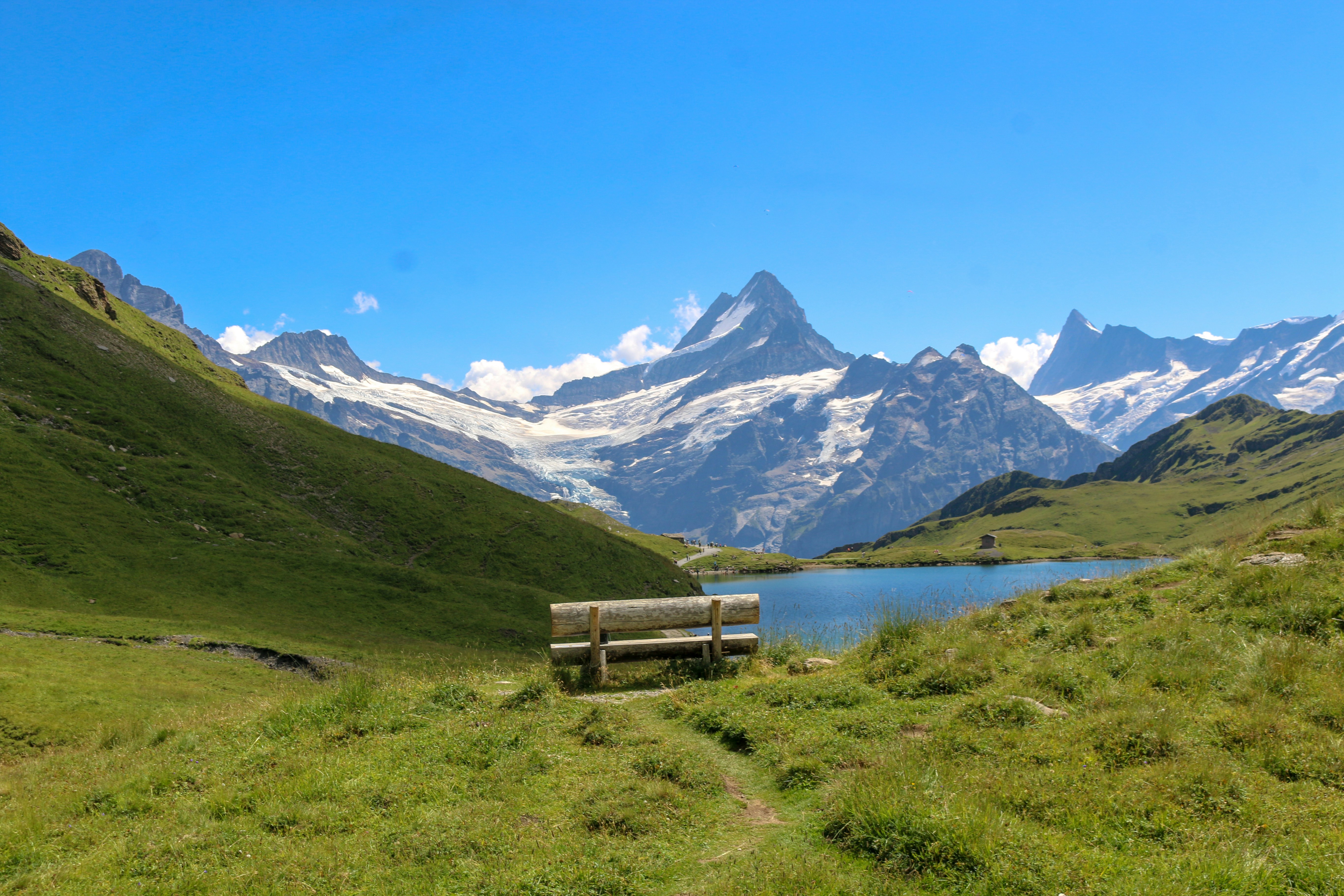 A wooden bench overlooking a blue alpine lake with snow-capped mountains in the background