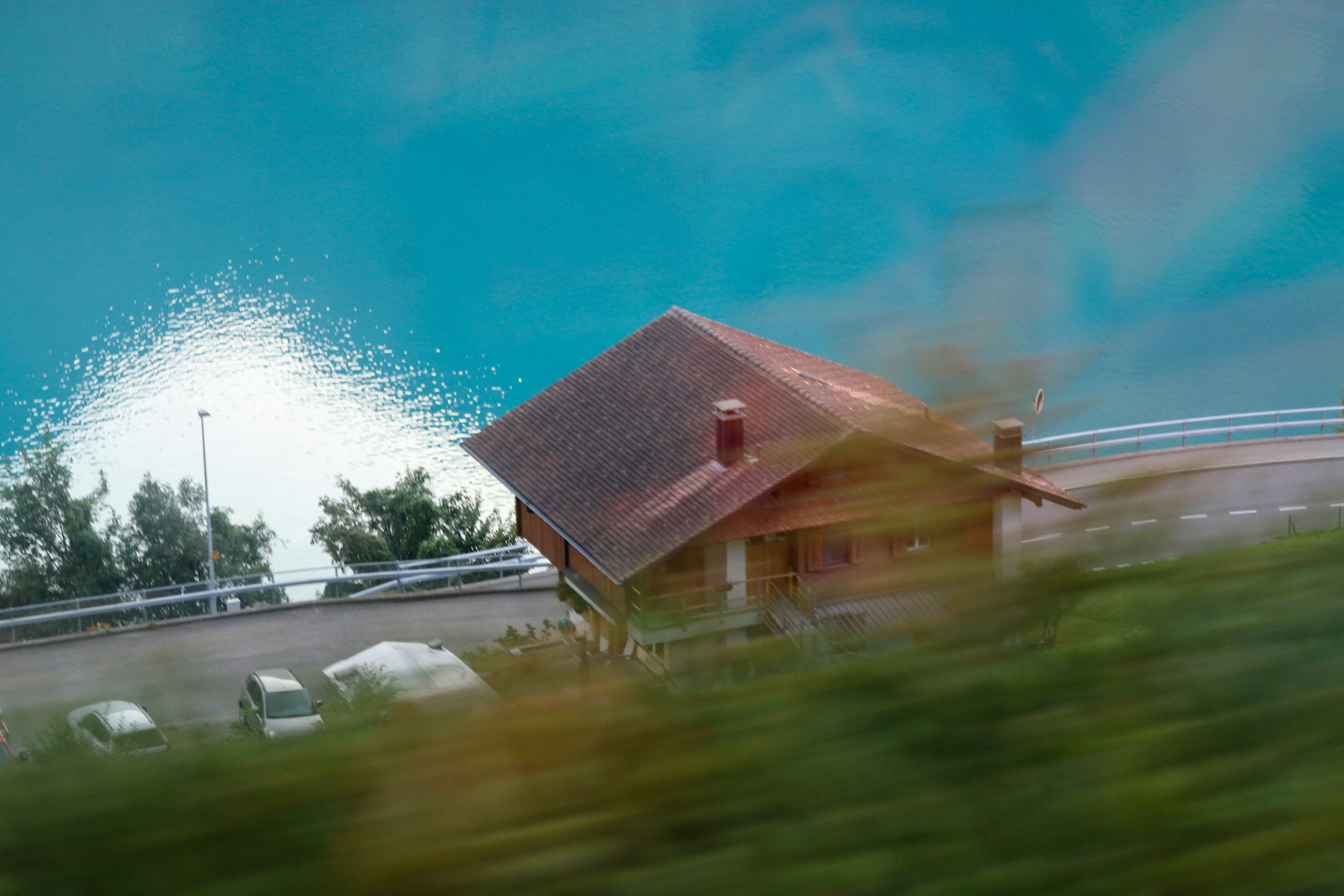 A wooden house beside a turquoise lake with a road and parked cars