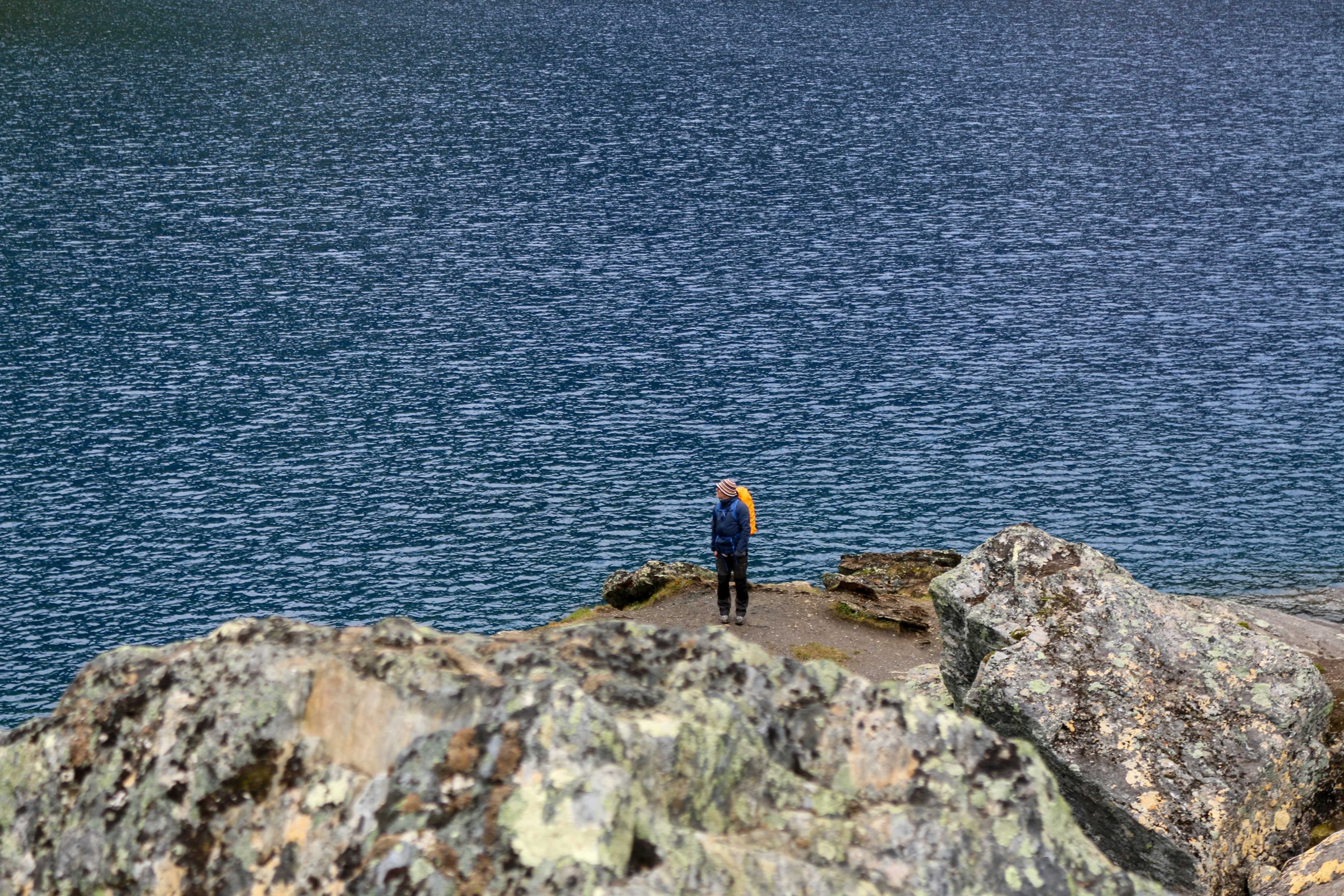 A person with a yellow backpack on a rocky outcrop above a blue lake
