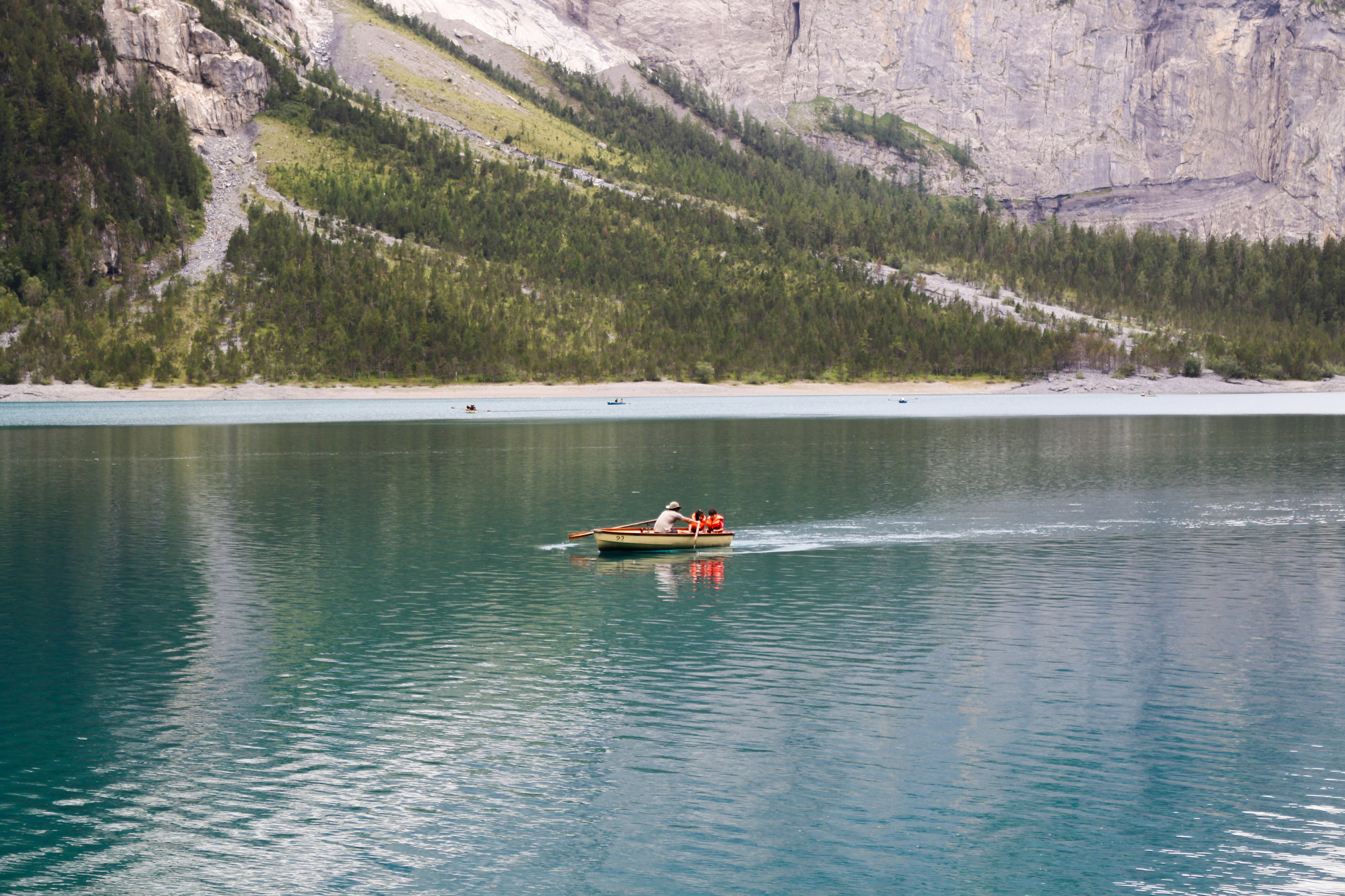 A small rowboat with people in orange life vests on a turquoise mountain lake