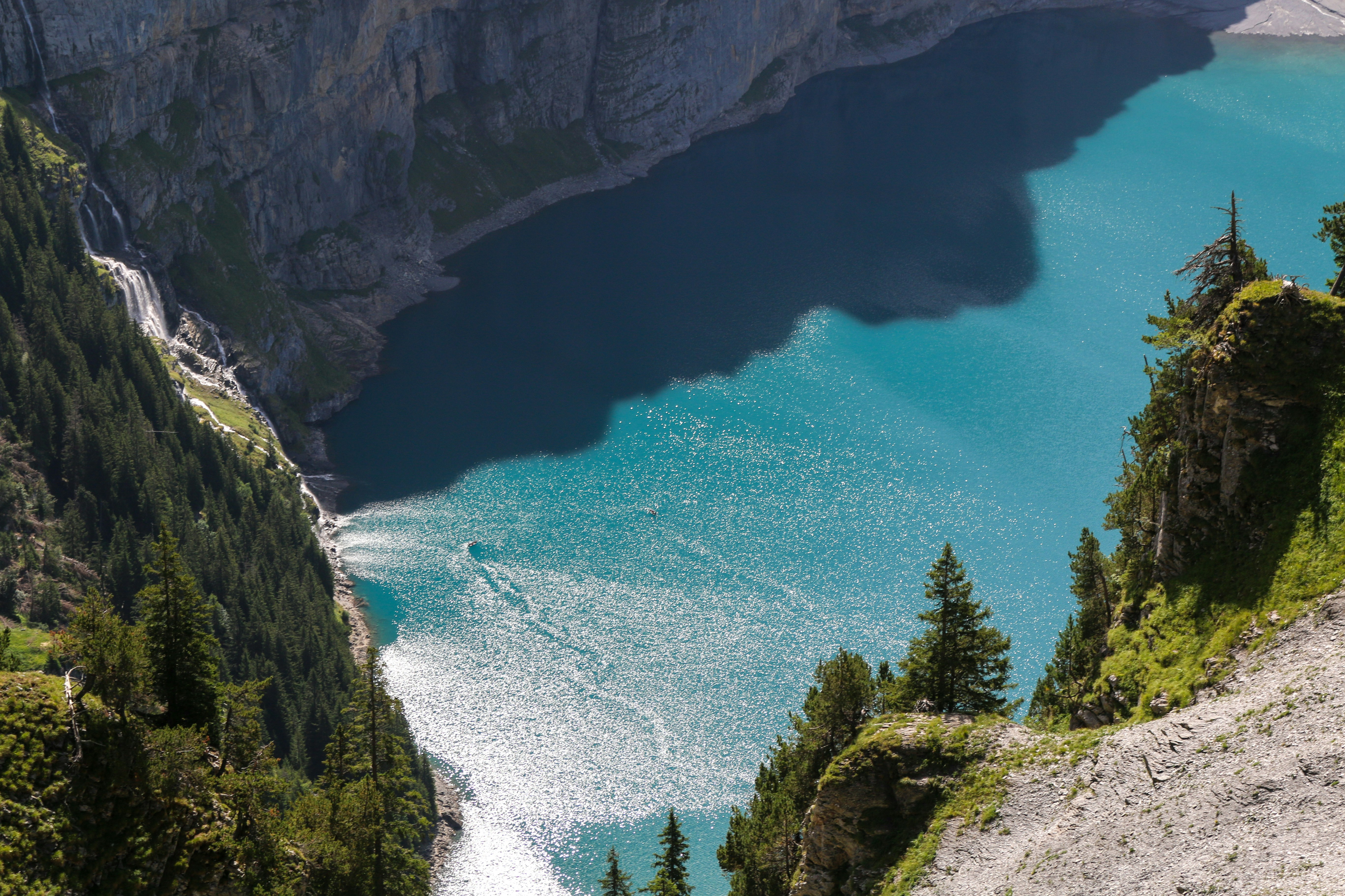 A turquoise lake below steep cliffs with a waterfall and pine trees