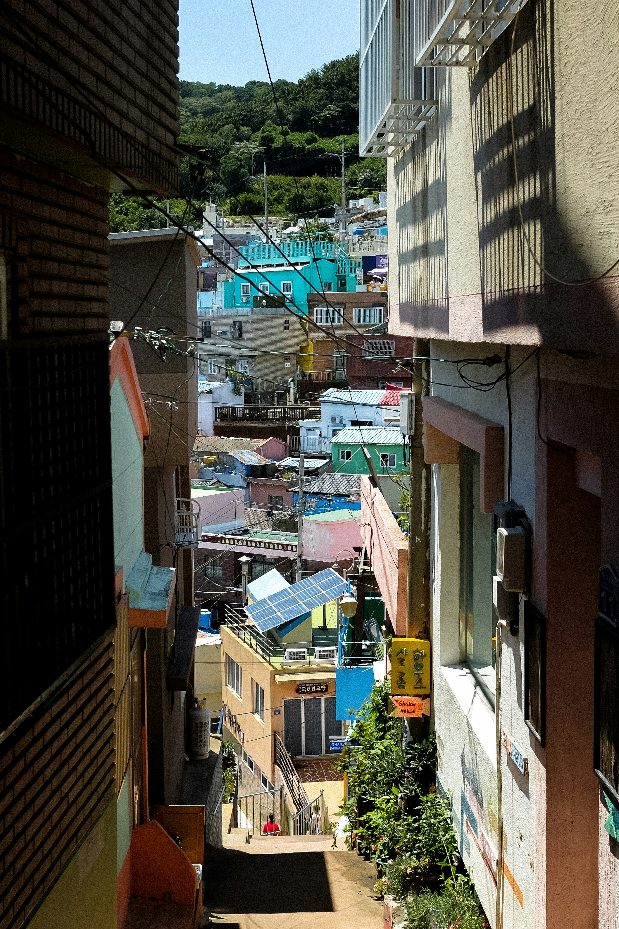 A narrow alleyway between colorful houses leading down to a hillside village