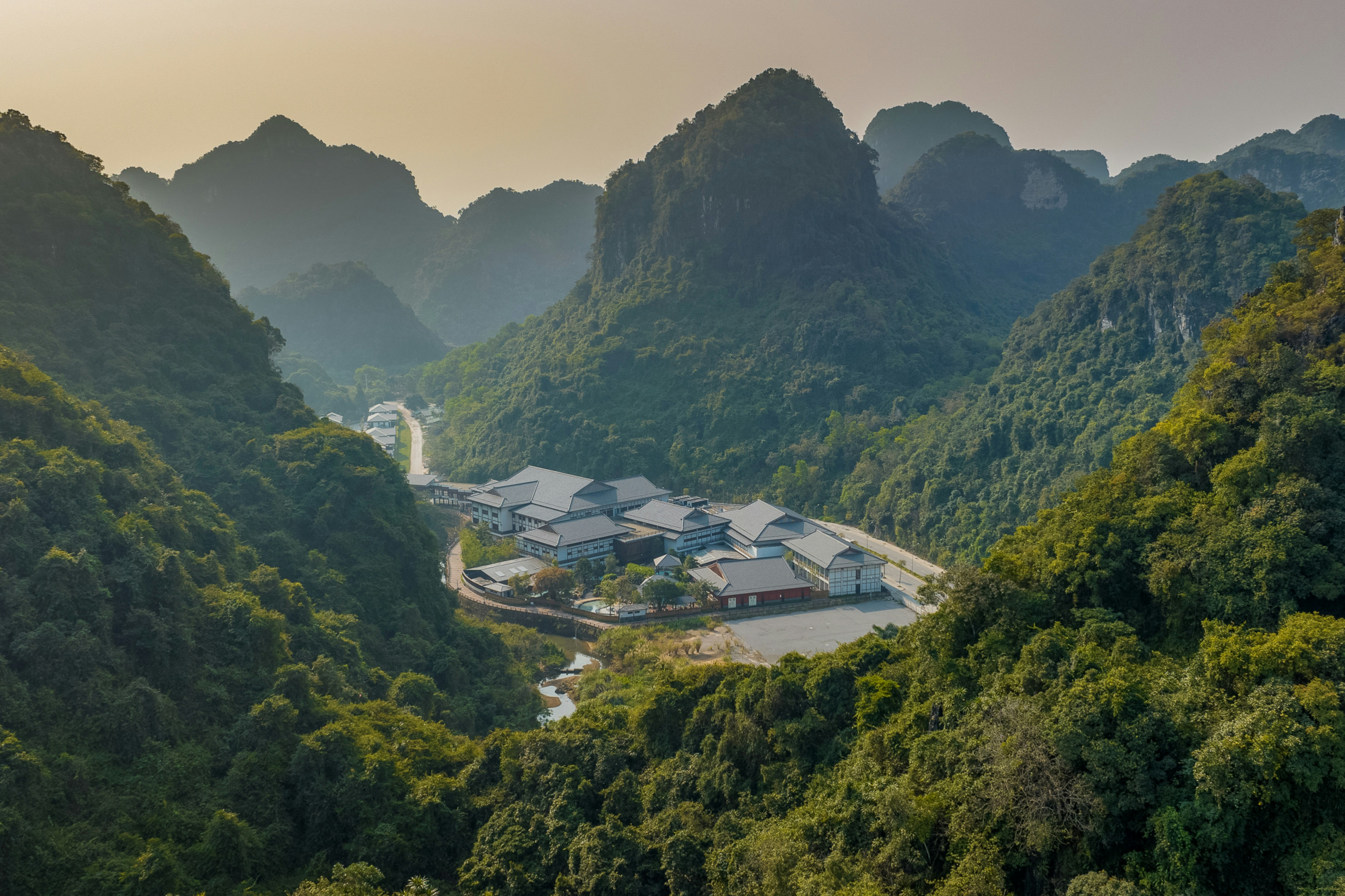 A complex of buildings nestled in a valley surrounded by steep forested karst mountains