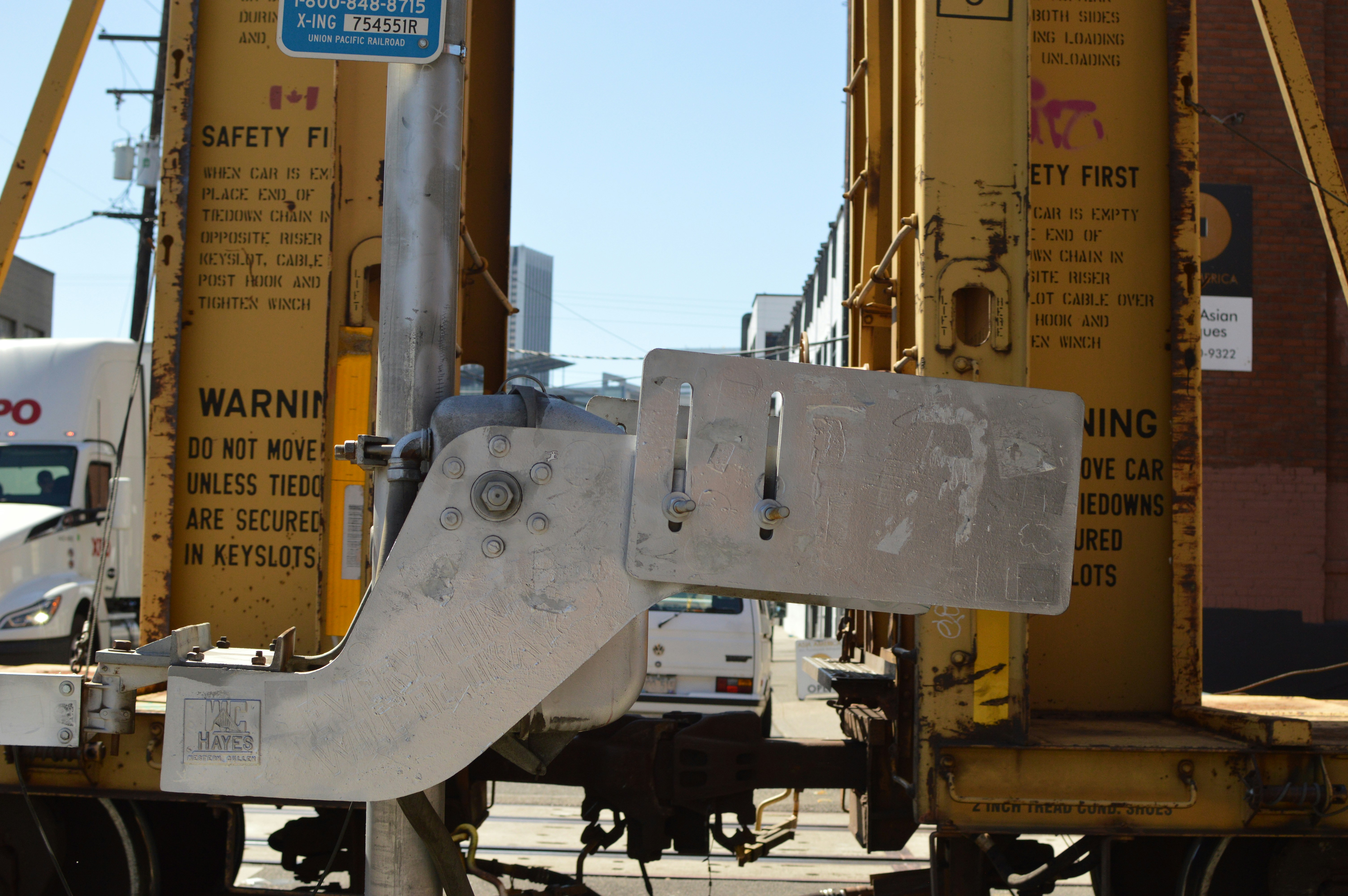 A metal Hayes derailer attached to a pole beside yellow railway freight cars