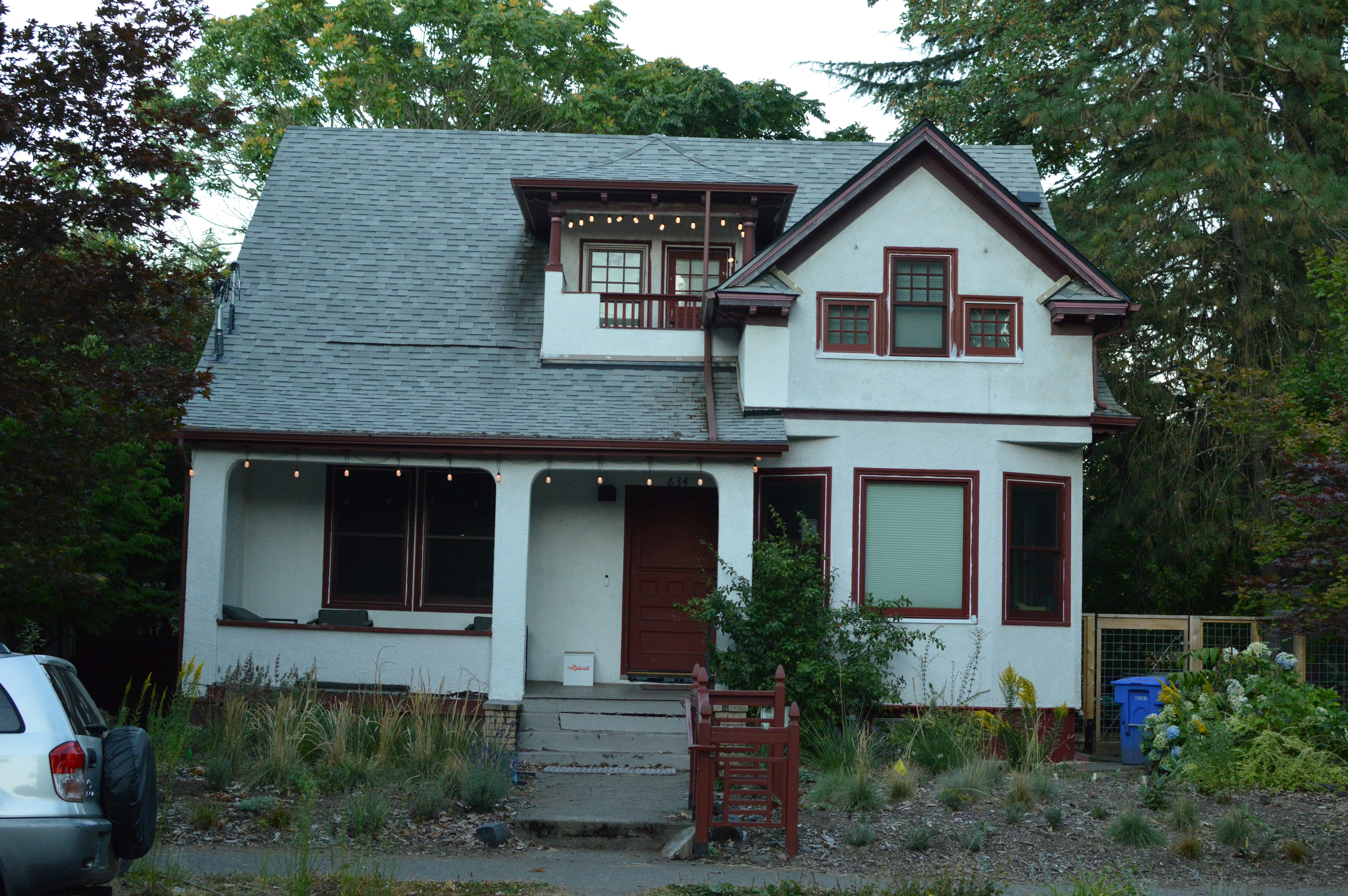 A white house with dark red trim and a grey shingled roof