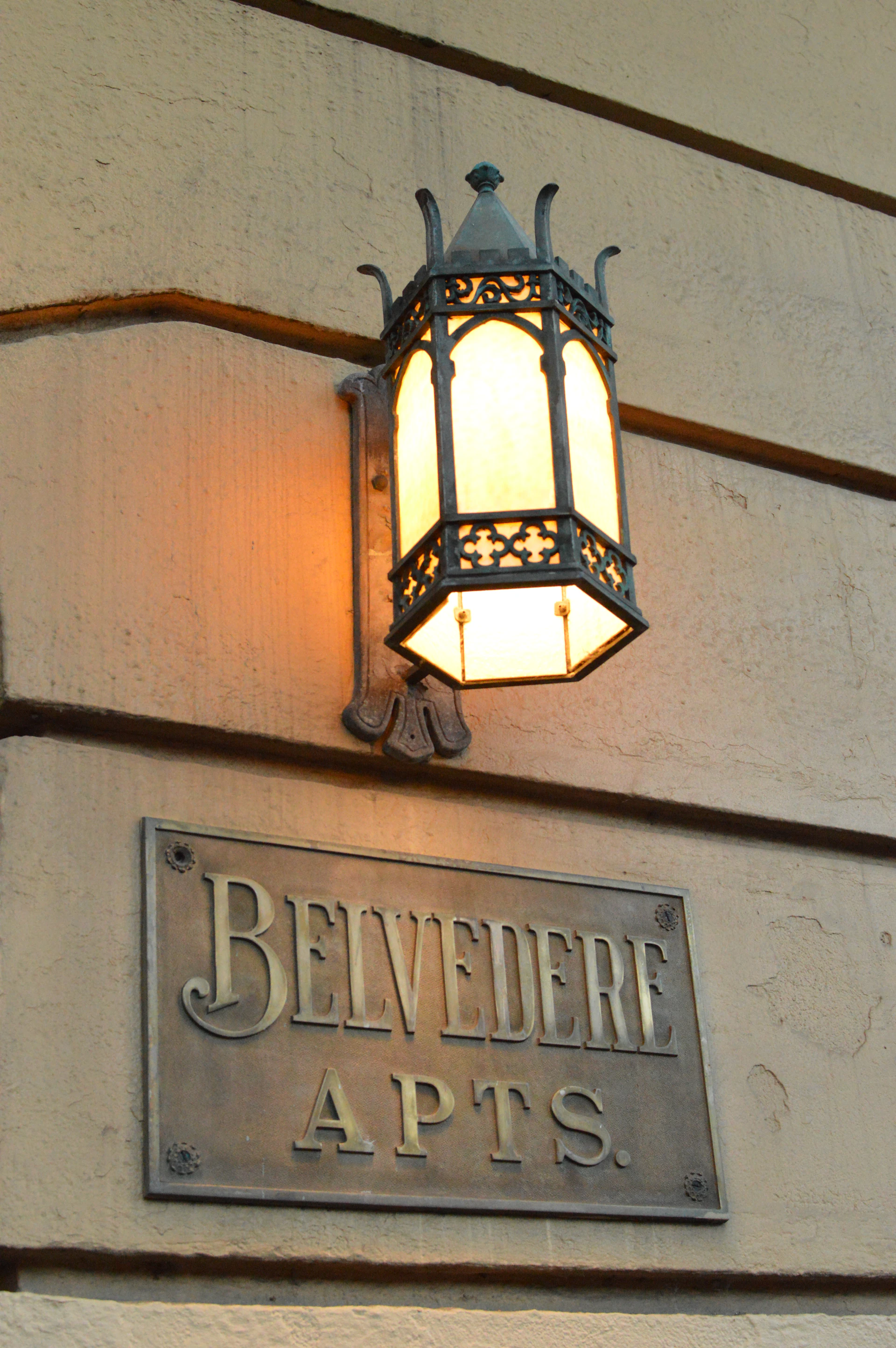 Metal building name plate reading Belvedere Apts mounted on a wall below a lantern