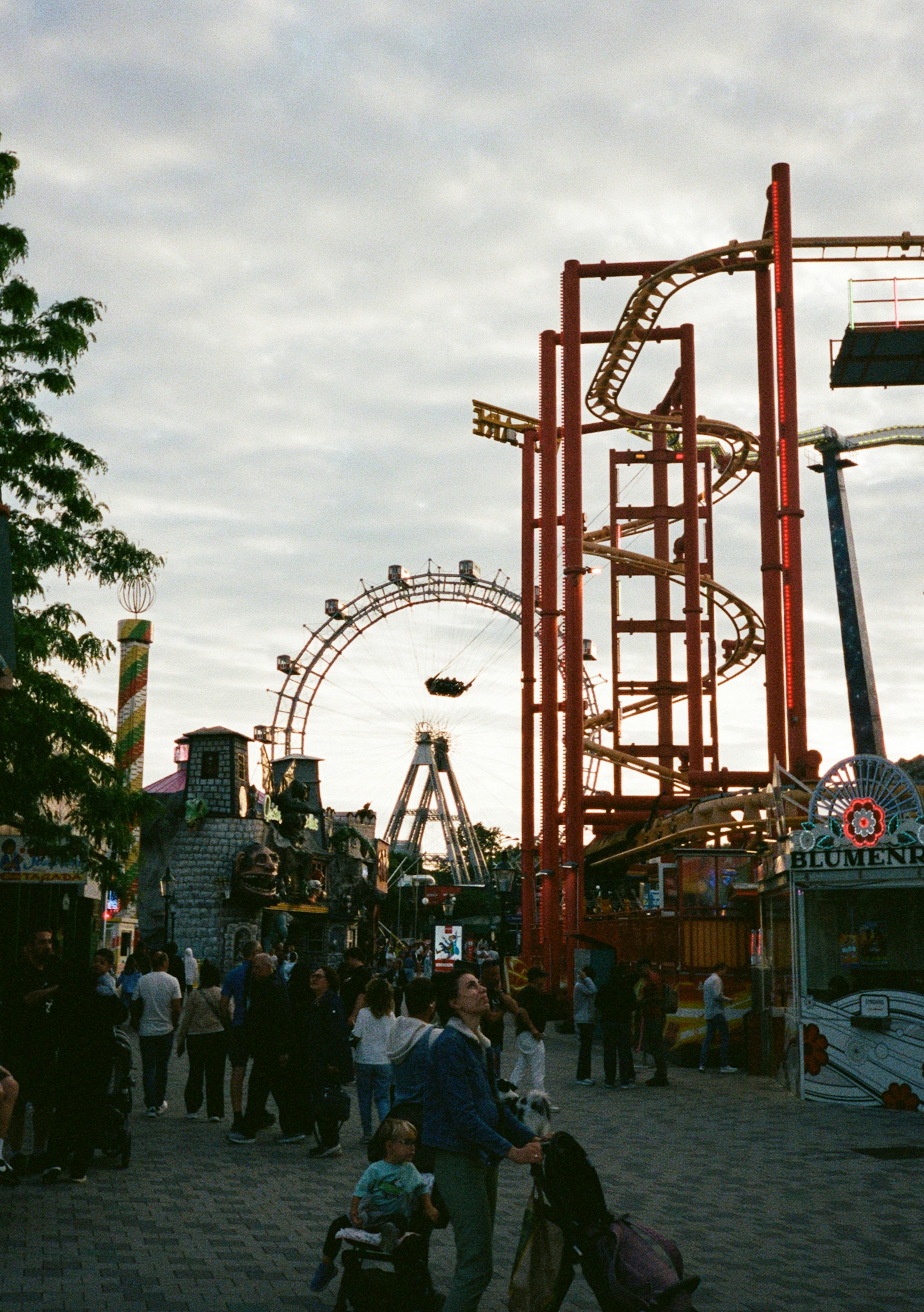 People walking through the Prater amusement park in Vienna with a ferris wheel