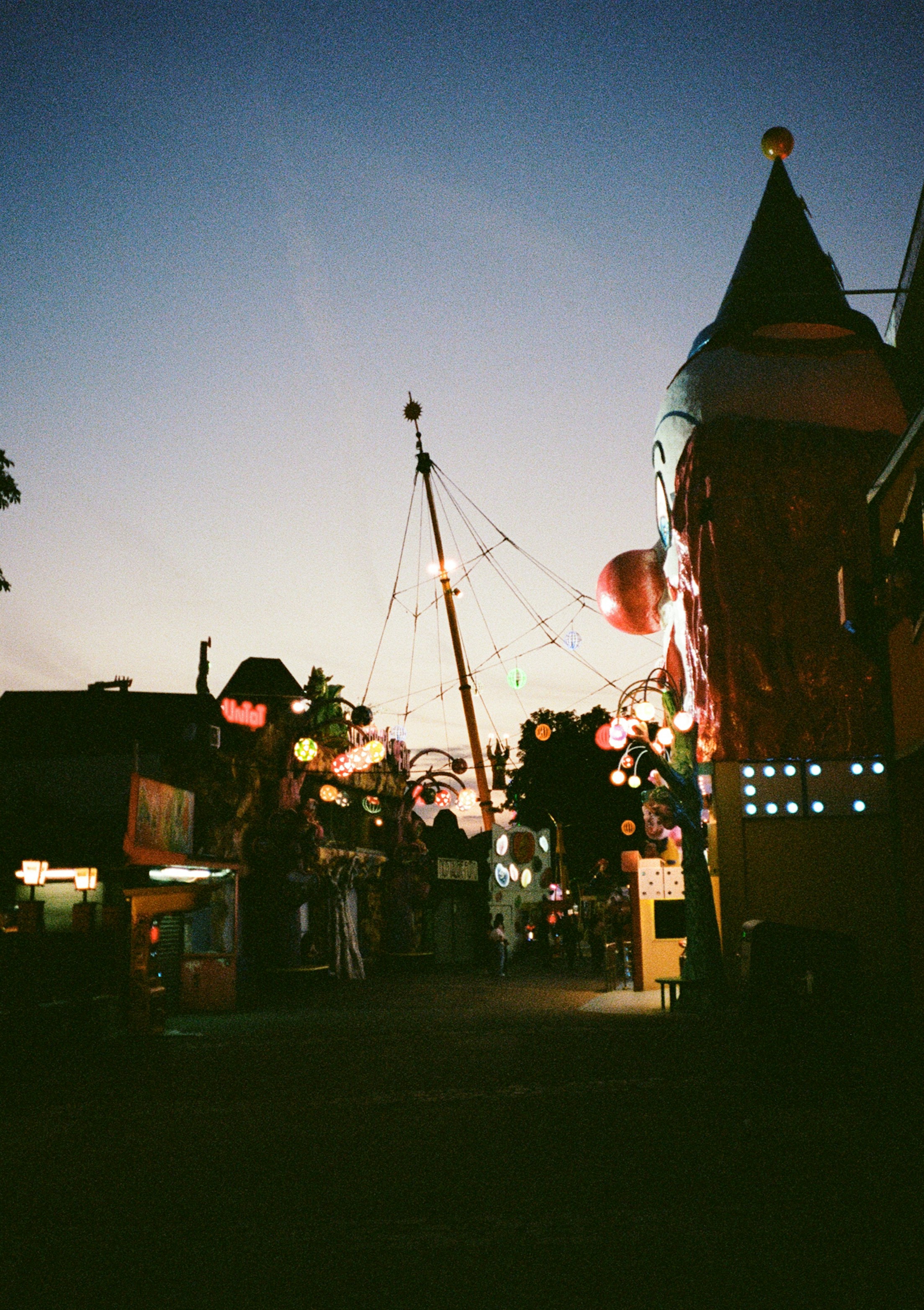 Amusement park rides and a clown facade at dusk in Vienna, Austria