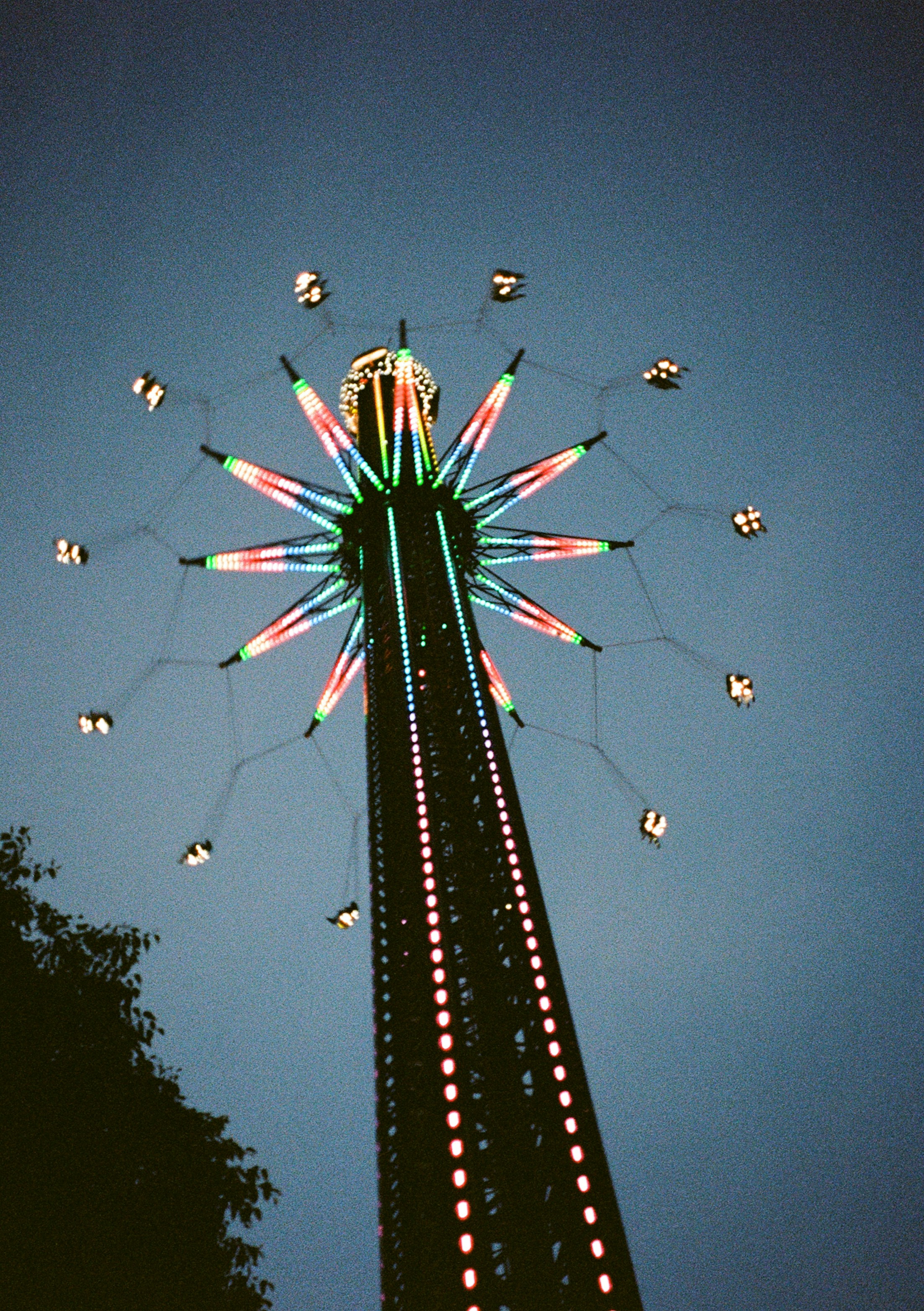 A tall illuminated swing ride spinning against a dark blue evening sky in Vienna