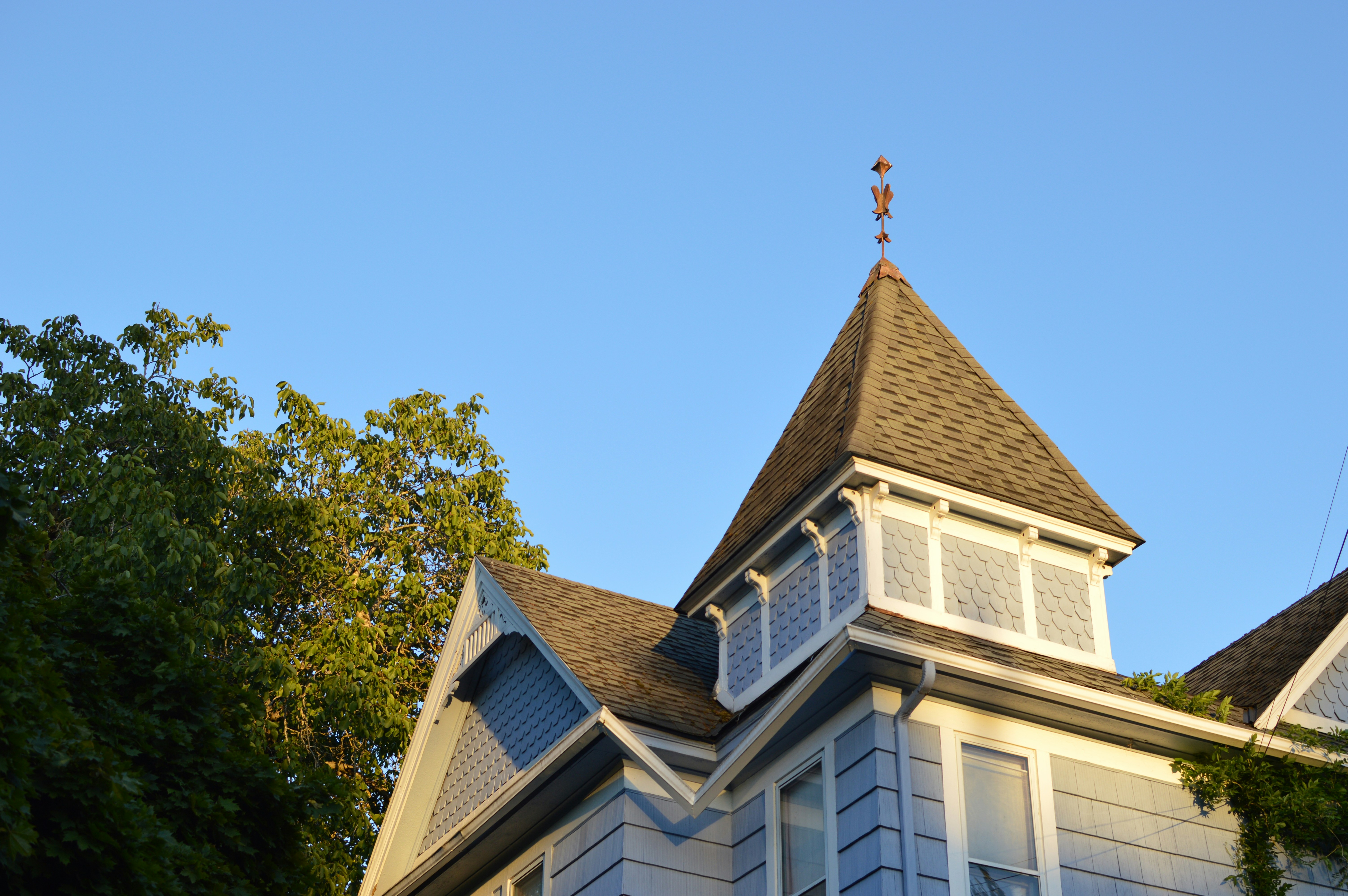 A blue Victorian house with a shingled turret under a clear blue sky