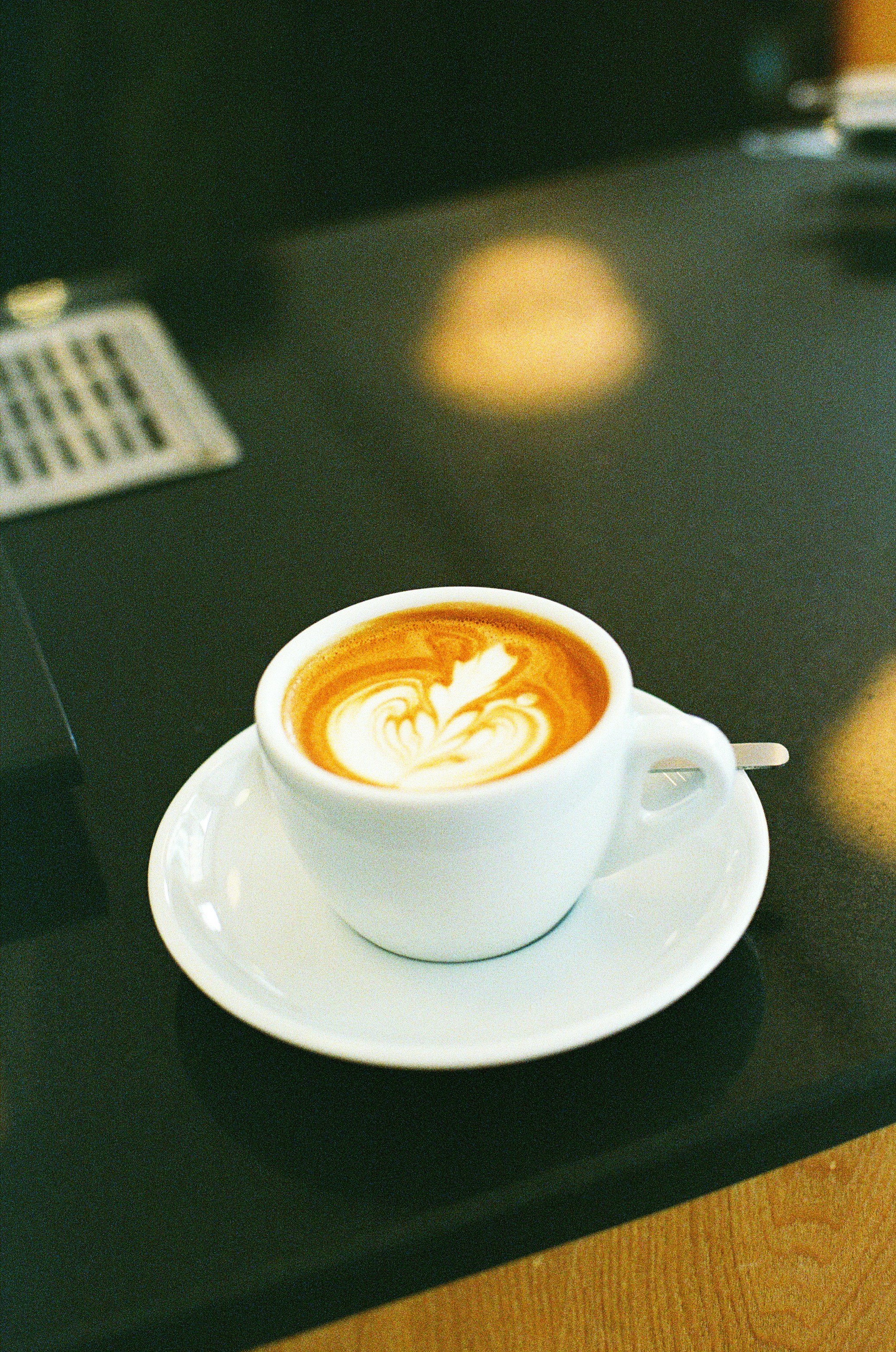 A white cup of latte with leaf latte art on a black surface
